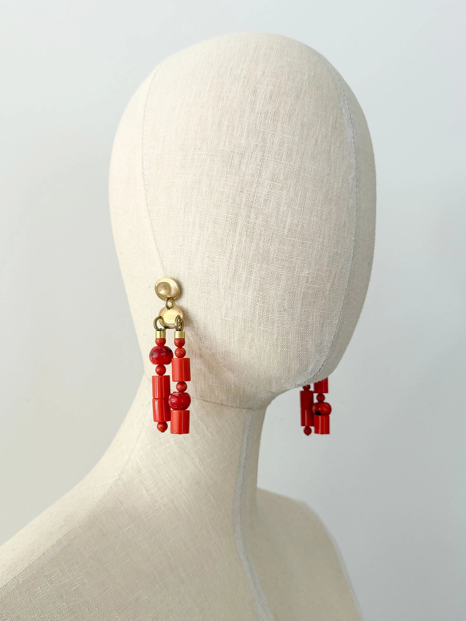 A pair of statement chandelier earrings featuring brass metal discs with vibrant red coral and resin beads by Canadian jewelry designer Michelle Ross