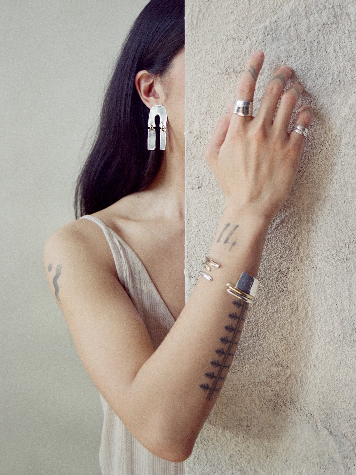 Woman wearing modern earrings, rings, and a bracelet with tattoos on her arm