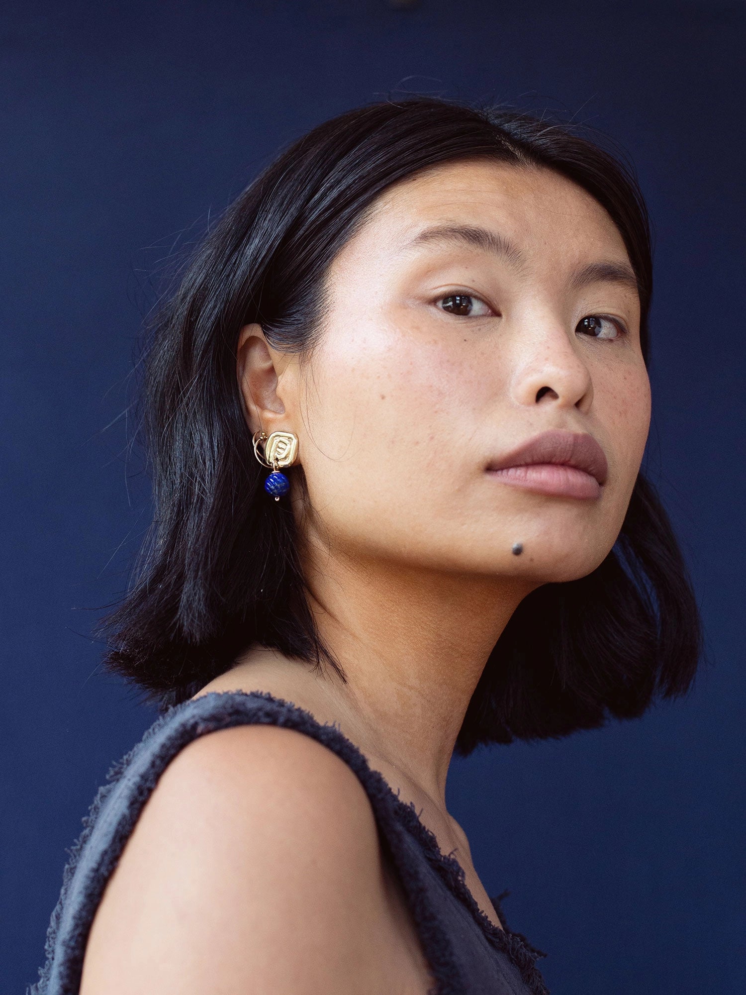 A woman wears a pair of hand-formed brass spiral drop earrings with lapis lazuli beaded stone by Canadian jewelry designer Michelle Ross