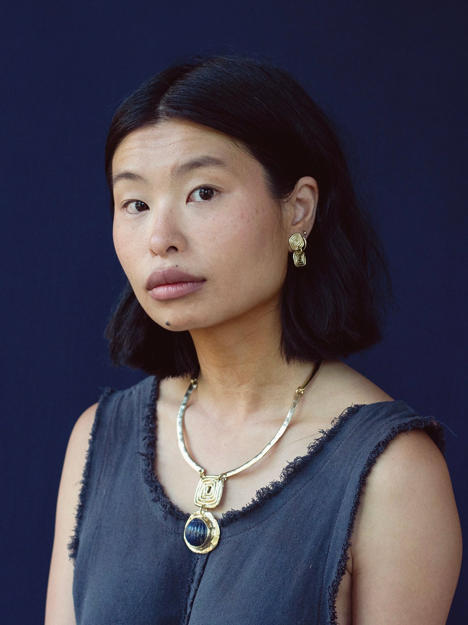 A woman wears a solid brass collar necklace with a lapis lazuli pendant by Canadian jewelry designer Michelle Ross