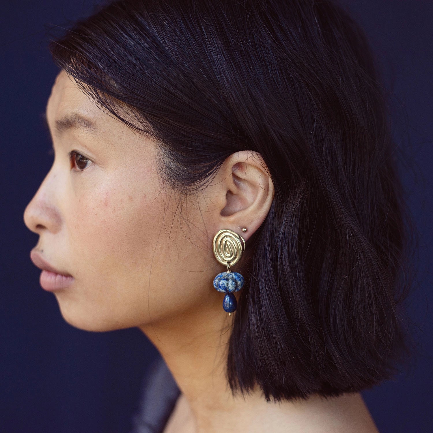 A woman wears a pair of hand-formed brass spiral earrings with lapis lazuli beaded stone drop style by Canadian jewelry designer Michelle Ross