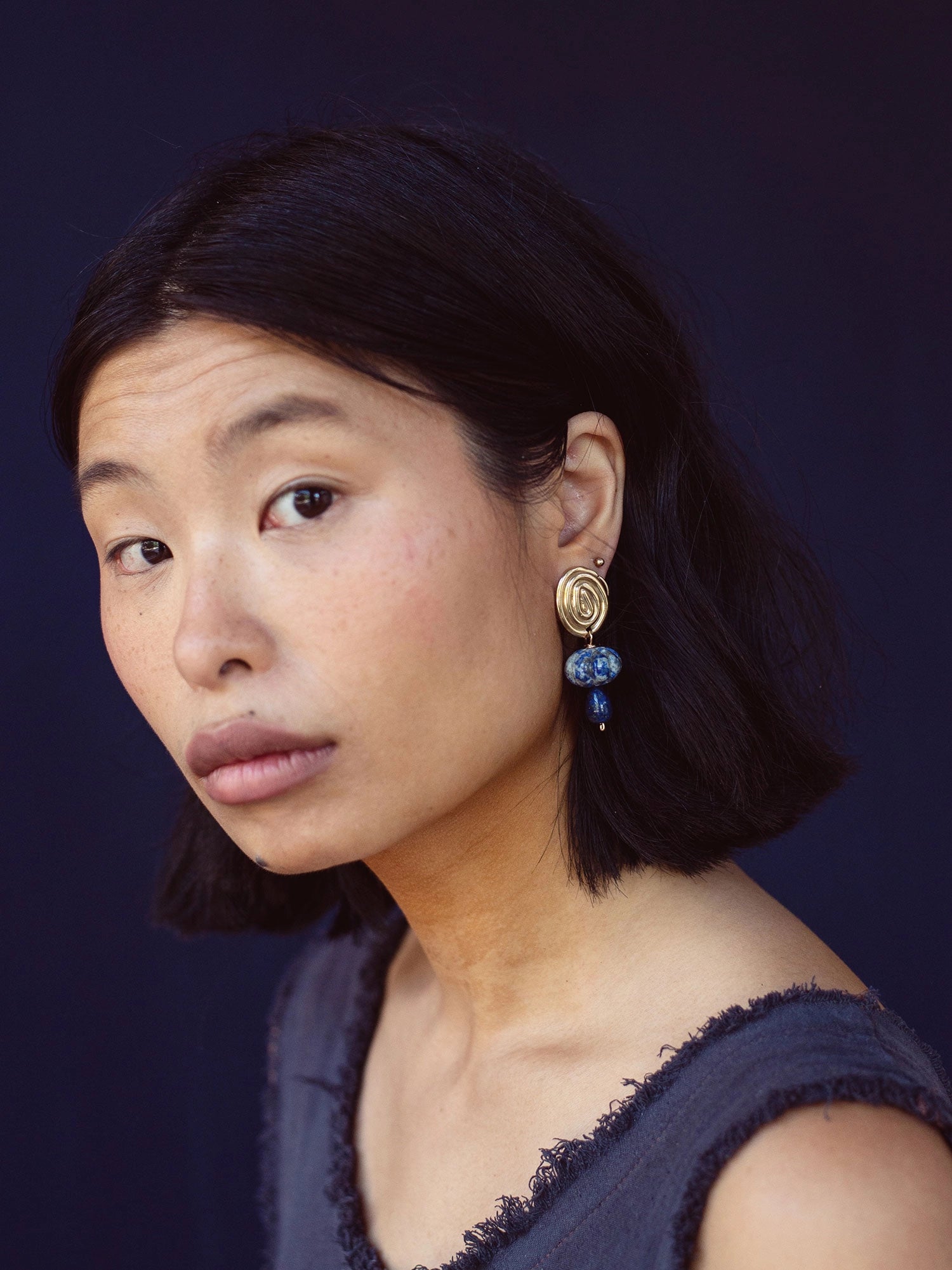 A woman wears a pair of hand-formed brass spiral earrings with lapis lazuli beaded stone drop style by Canadian jewelry designer Michelle Ross