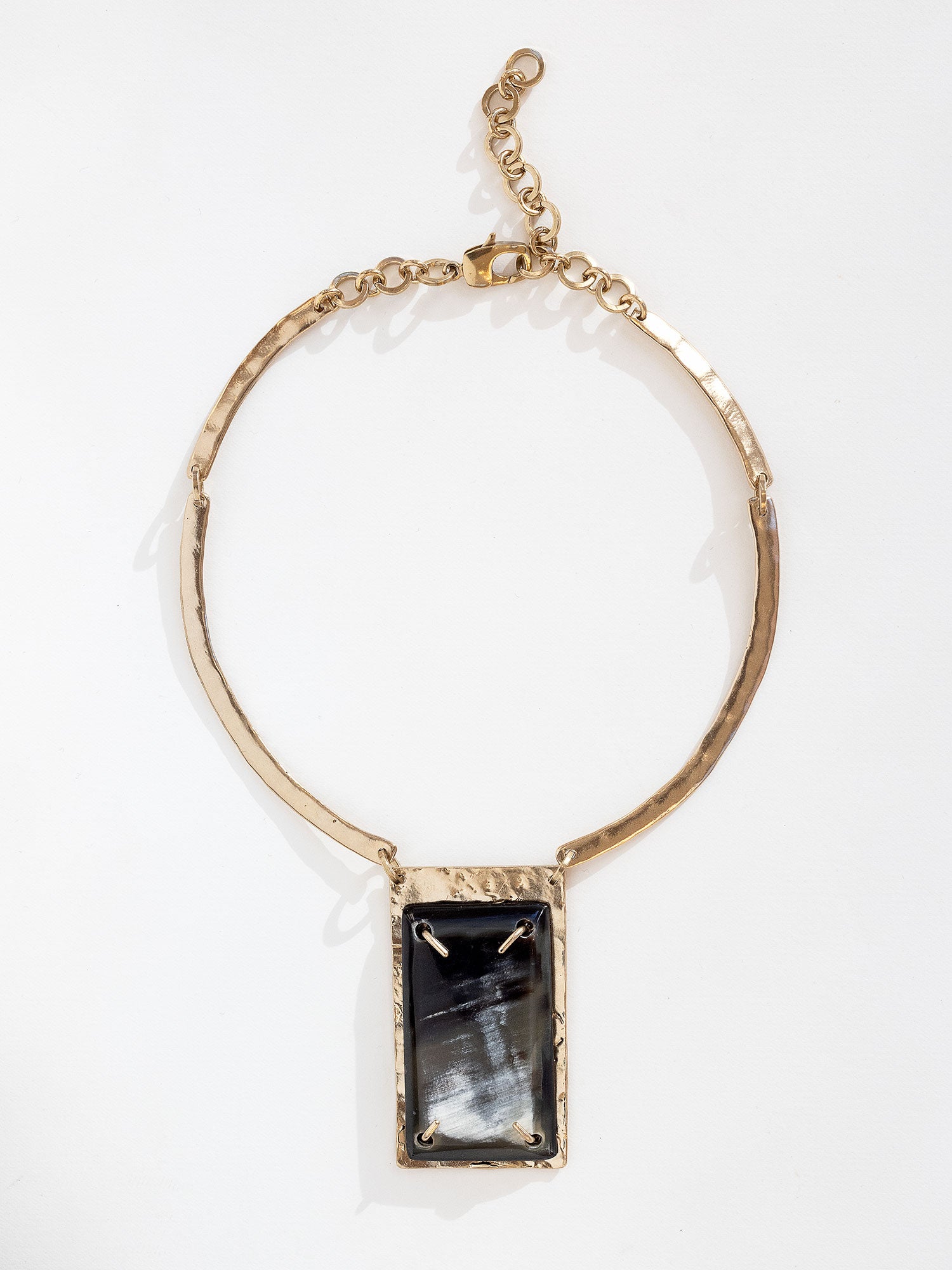 A solid brass collar necklace featuring a statement black horn pendant by Michelle Ross