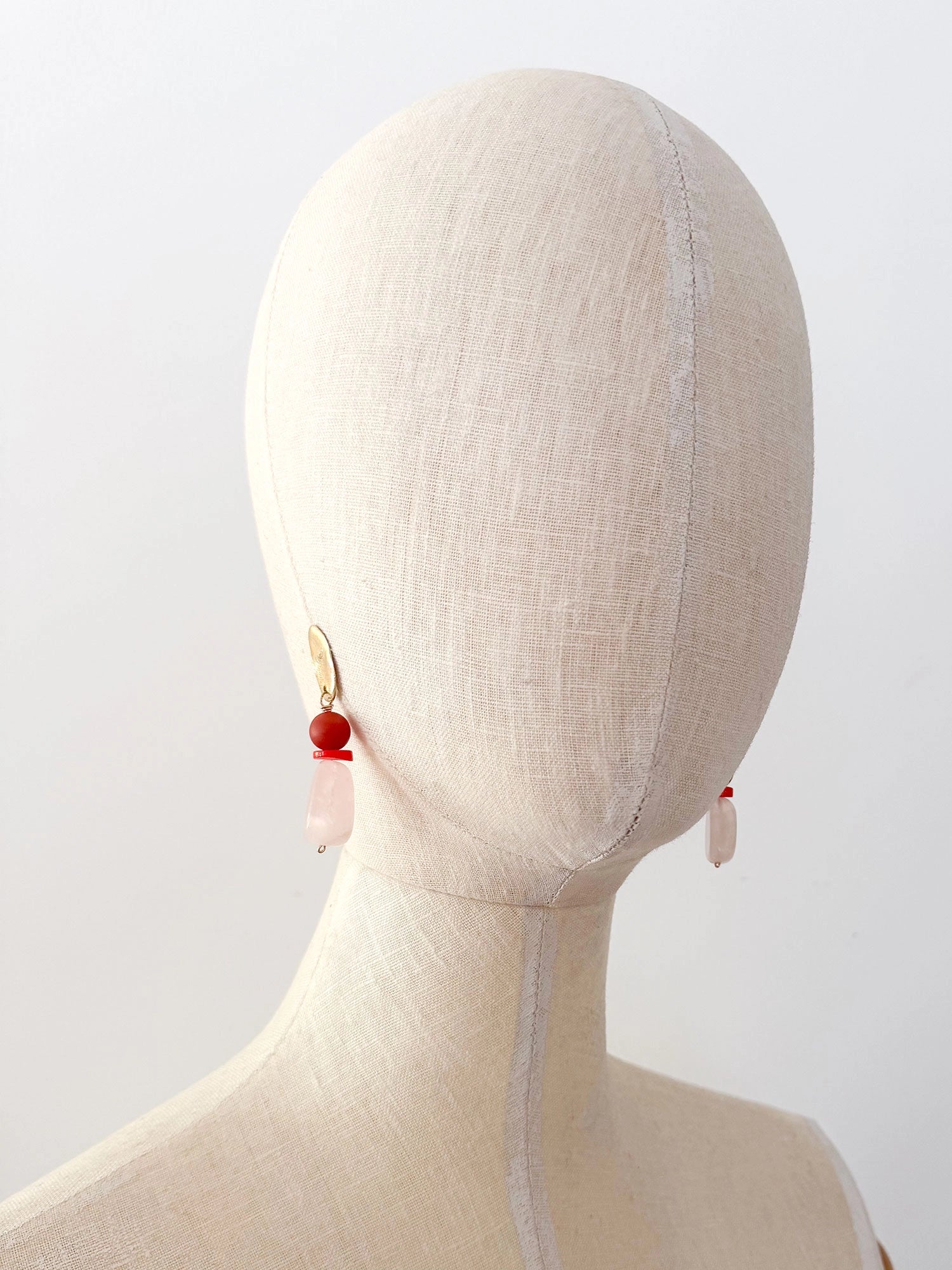 A pair of statement dangle earrings featuring textured brass tops, a round red carnelian bead, a small coral spacer, and a teardrop-shaped pale pink rose quartz bead by Canadian jewelry designer Michelle Ross.