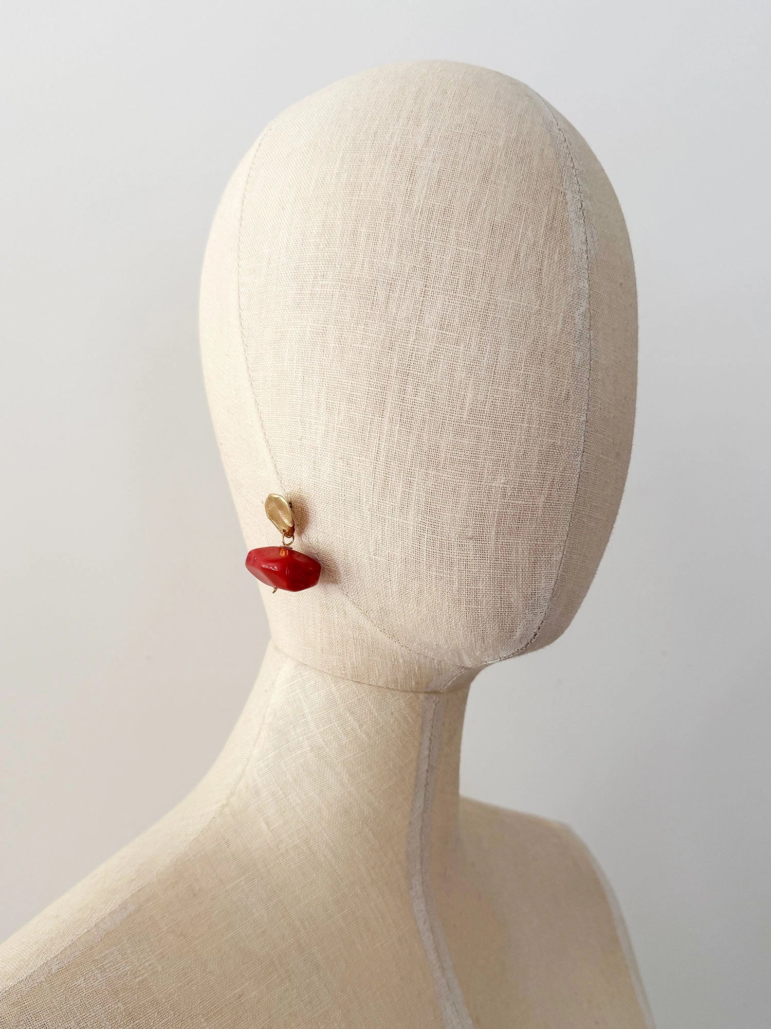 A pair of drop earrings featuring textured brass metal studs and large, polished red resin beaded drops by Canadian jewelry designer Michelle Ross