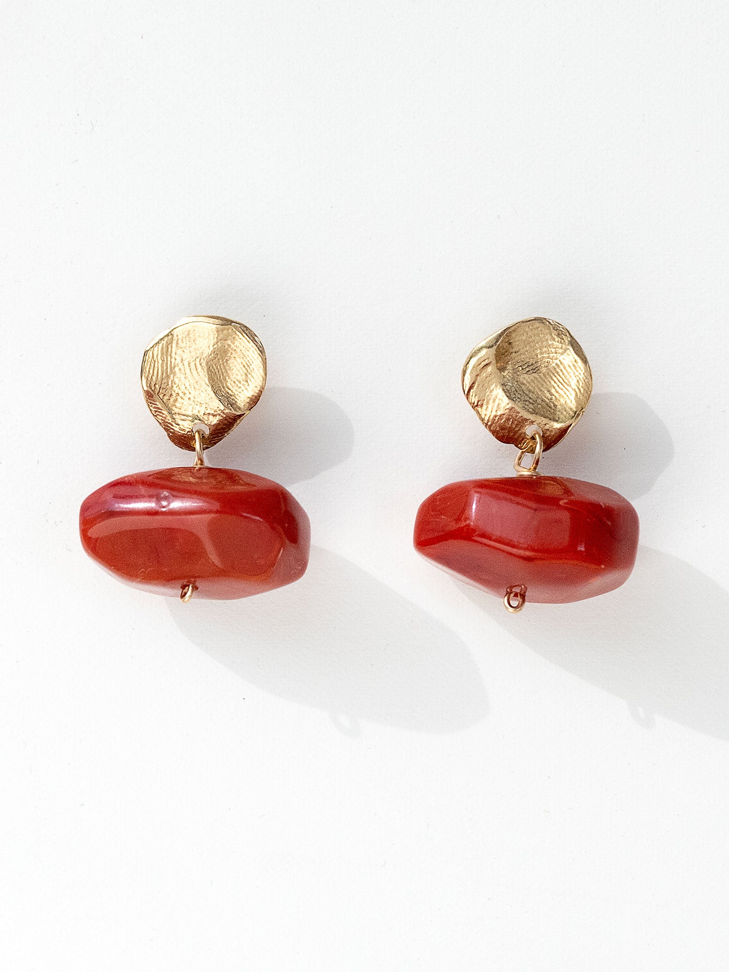A pair of drop earrings featuring textured brass metal studs and large, polished red resin beaded drops by Canadian jewelry designer Michelle Ross
