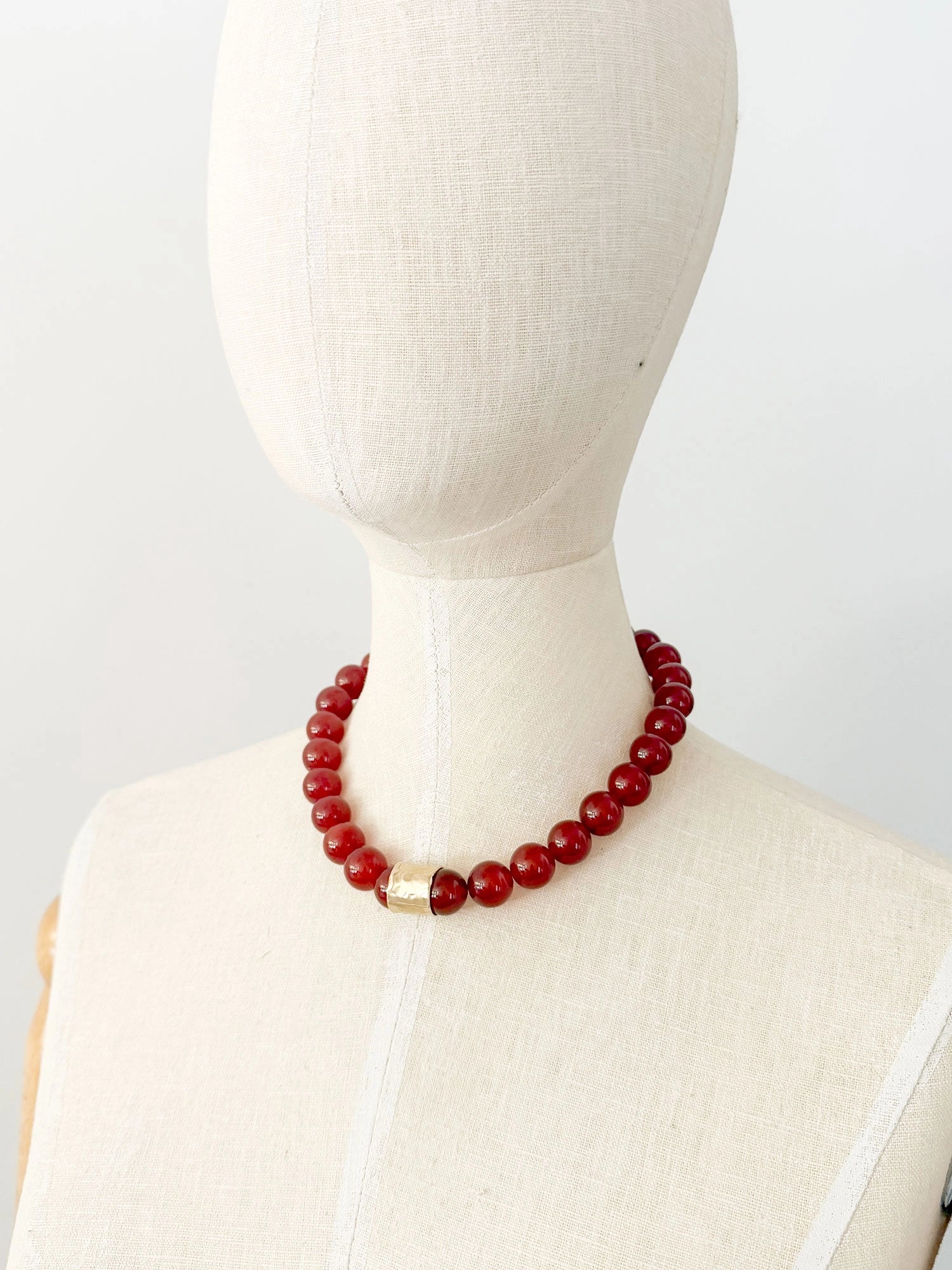 A beaded necklace featuring glossy red round carnelian beads and a textured brass accent piece by Canadian jewelry designer Michelle Ross