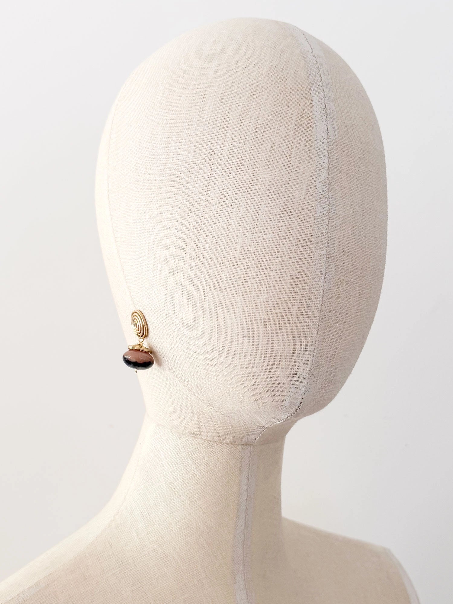 A pair of brass spiral drop earrings with marbled pink and black beads hanging below by Canadian jewelry designer Michelle Ross
