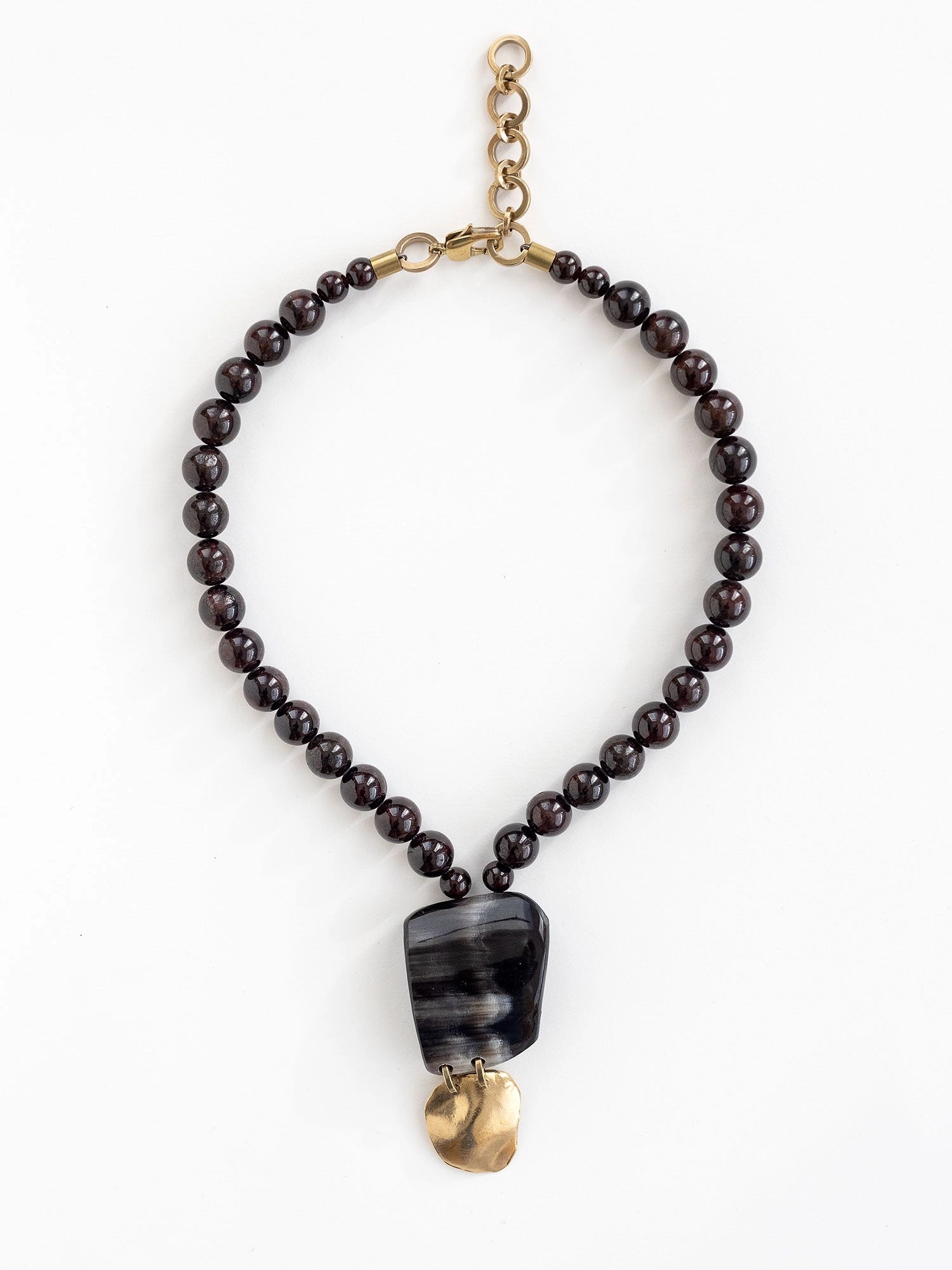 Necklace with garnet beads and a large black horn and brass pendant by Michelle Ross