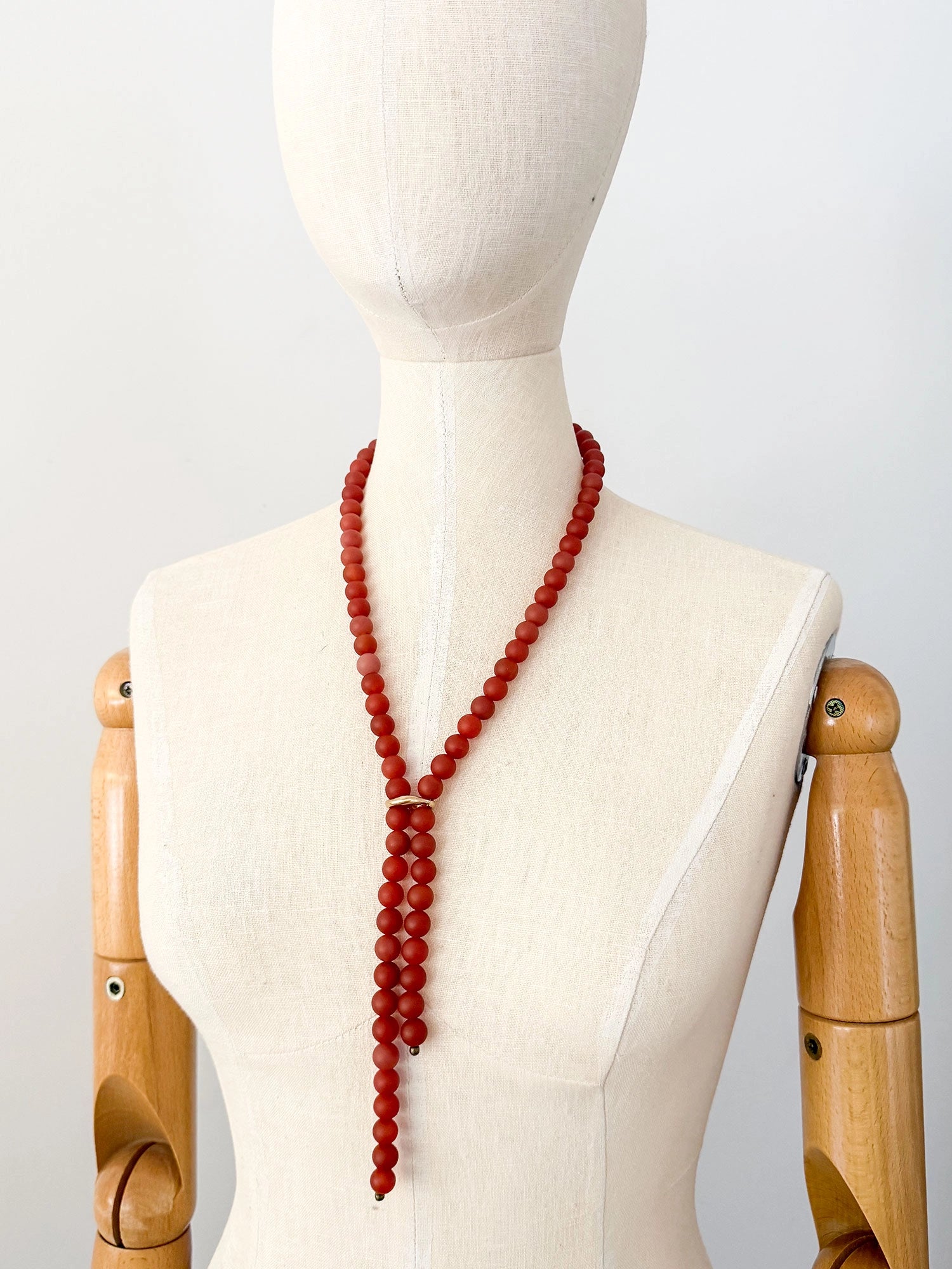 A beaded lariat style necklace made of round carnelian red beads with brass details by Canadian jewelry designer Michelle Ross