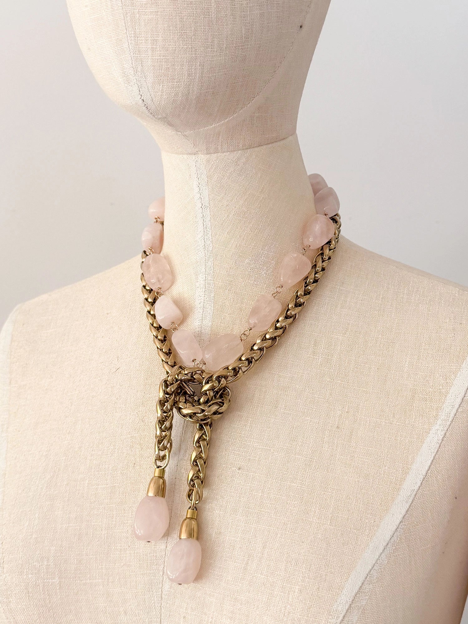 A brass chain lariat necklace knotted with two dangling light pink rose quartz teardrop-shaped beads at the bottom with a beaded rose quartz necklace layered over top by Canadian jewelry designer Michelle Ross