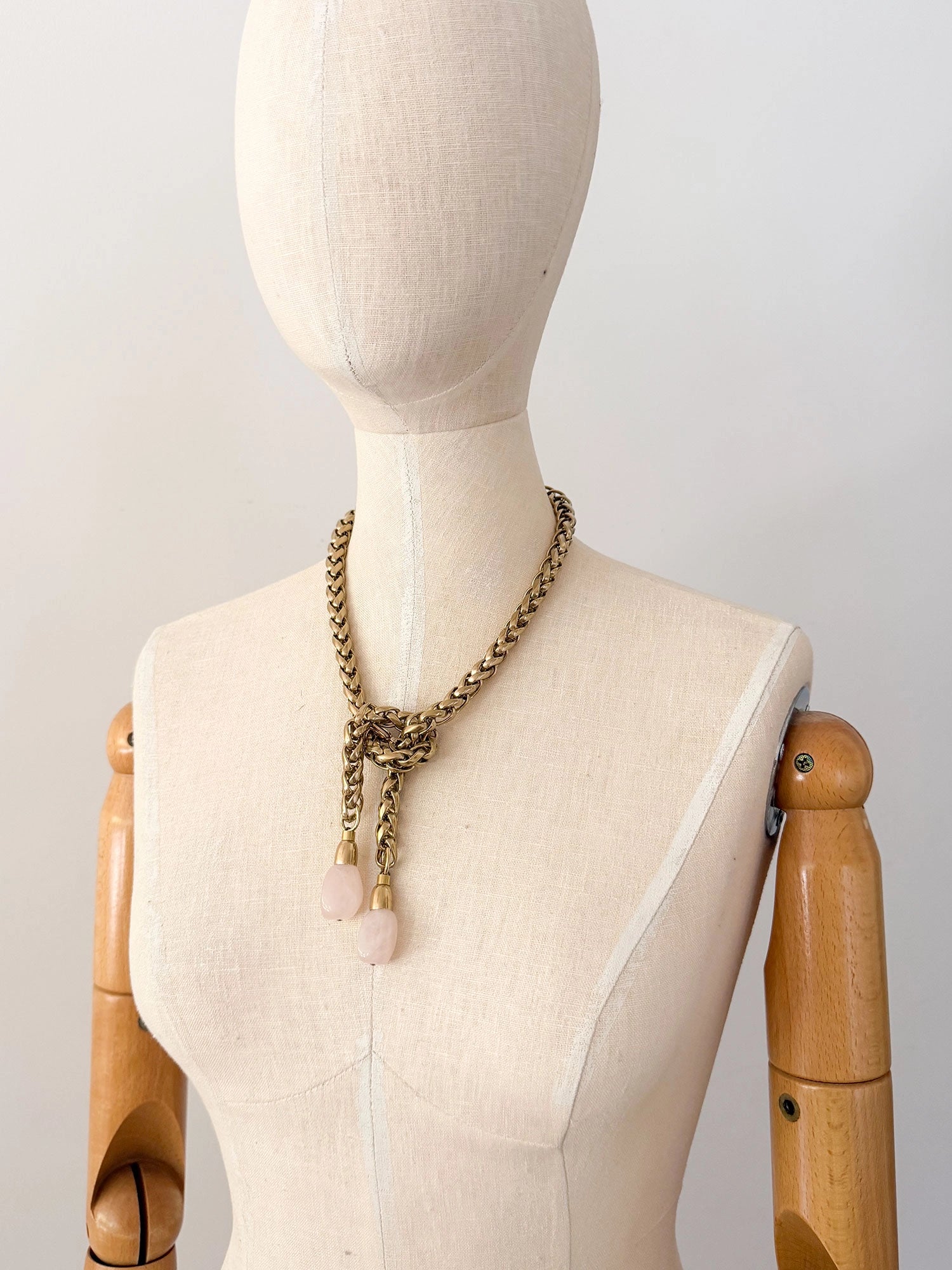 A brass chain lariat necklace knotted with two dangling light pink rose quartz teardrop-shaped beads at the bottom by Canadian jewelry designer Michelle Ross