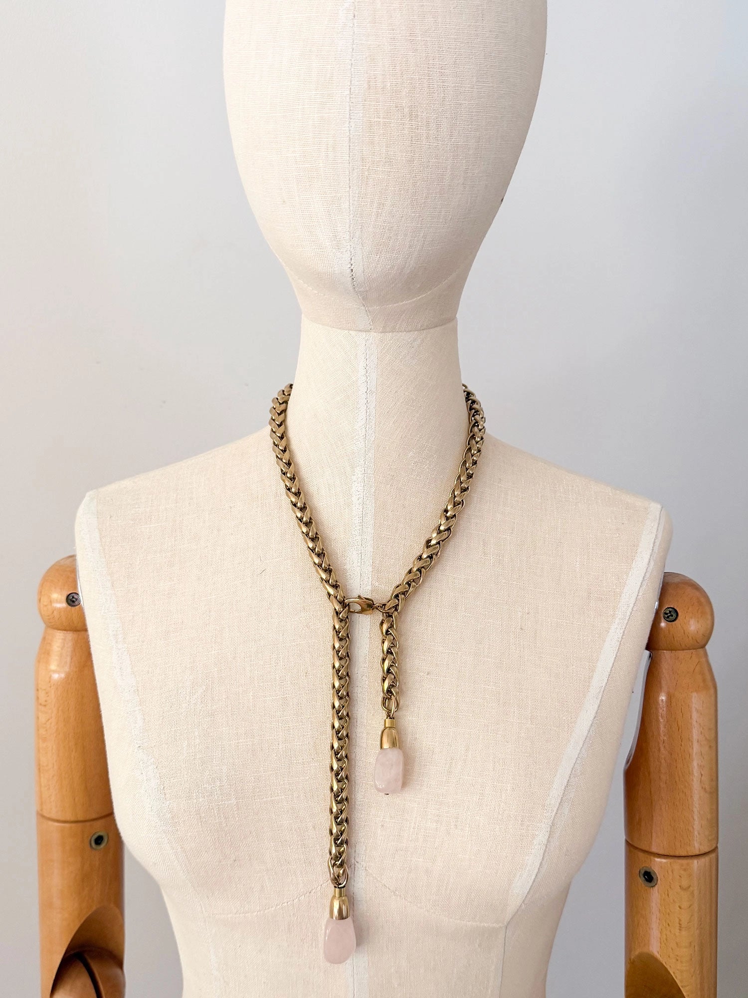 A brass chain lariat necklace knotted with two dangling light pink rose quartz teardrop-shaped beads at the bottom by Canadian jewelry designer Michelle Ross