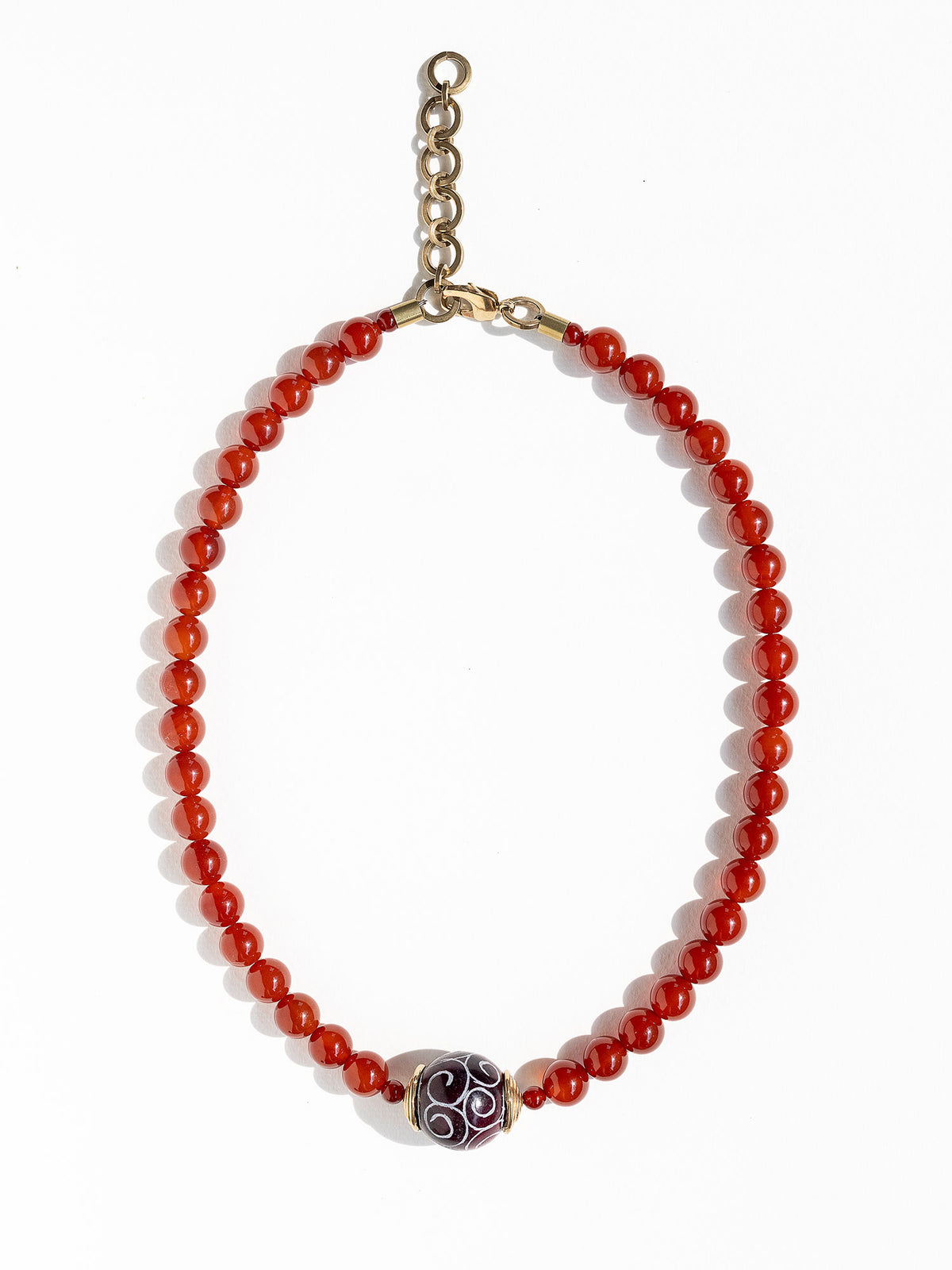 A beaded necklace made of small carnelian beads with a decorative dark brown and white patterned carved agate pendant and brass details by Canadian Jewelry designer Michelle Ross
