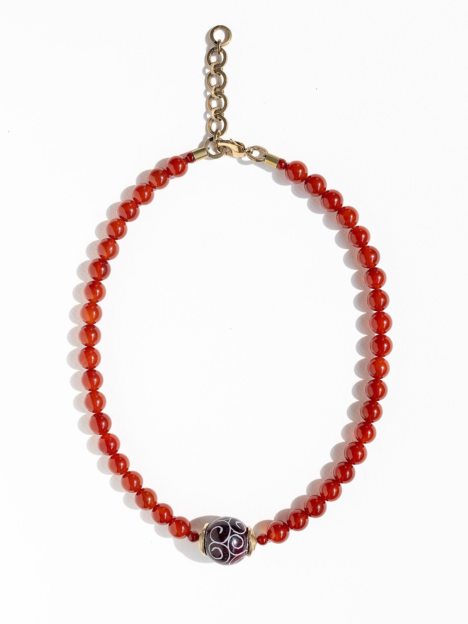 A beaded necklace made of small carnelian beads with a decorative dark brown and white patterned carved agate pendant and brass details by Canadian Jewelry designer Michelle Ross