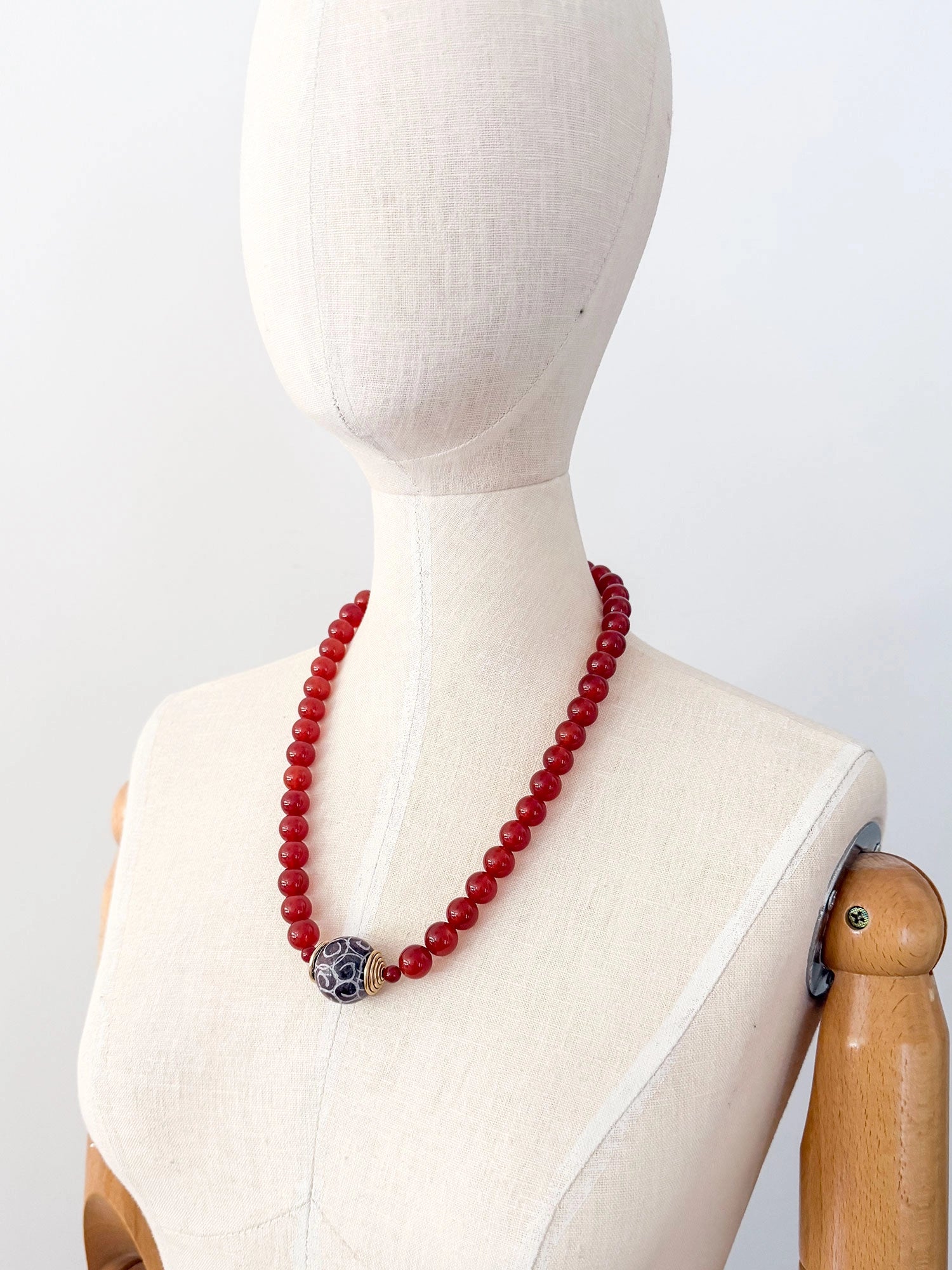 A beaded necklace made of small carnelian beads with a decorative dark brown and white patterned carved agate pendant and brass details by Canadian Jewelry designer Michelle Ross