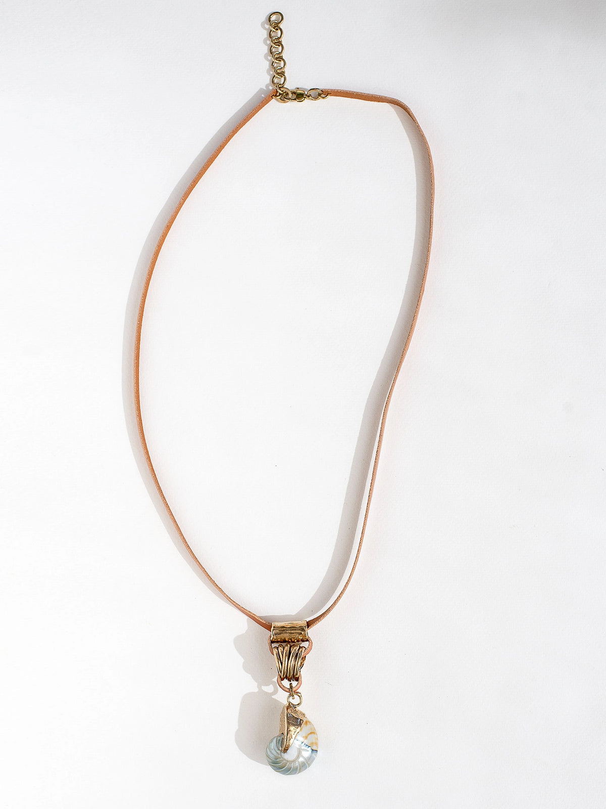 A tan leather long necklace with a brass and seashell statement pendant by Canadian jewelry designer Michelle Ross