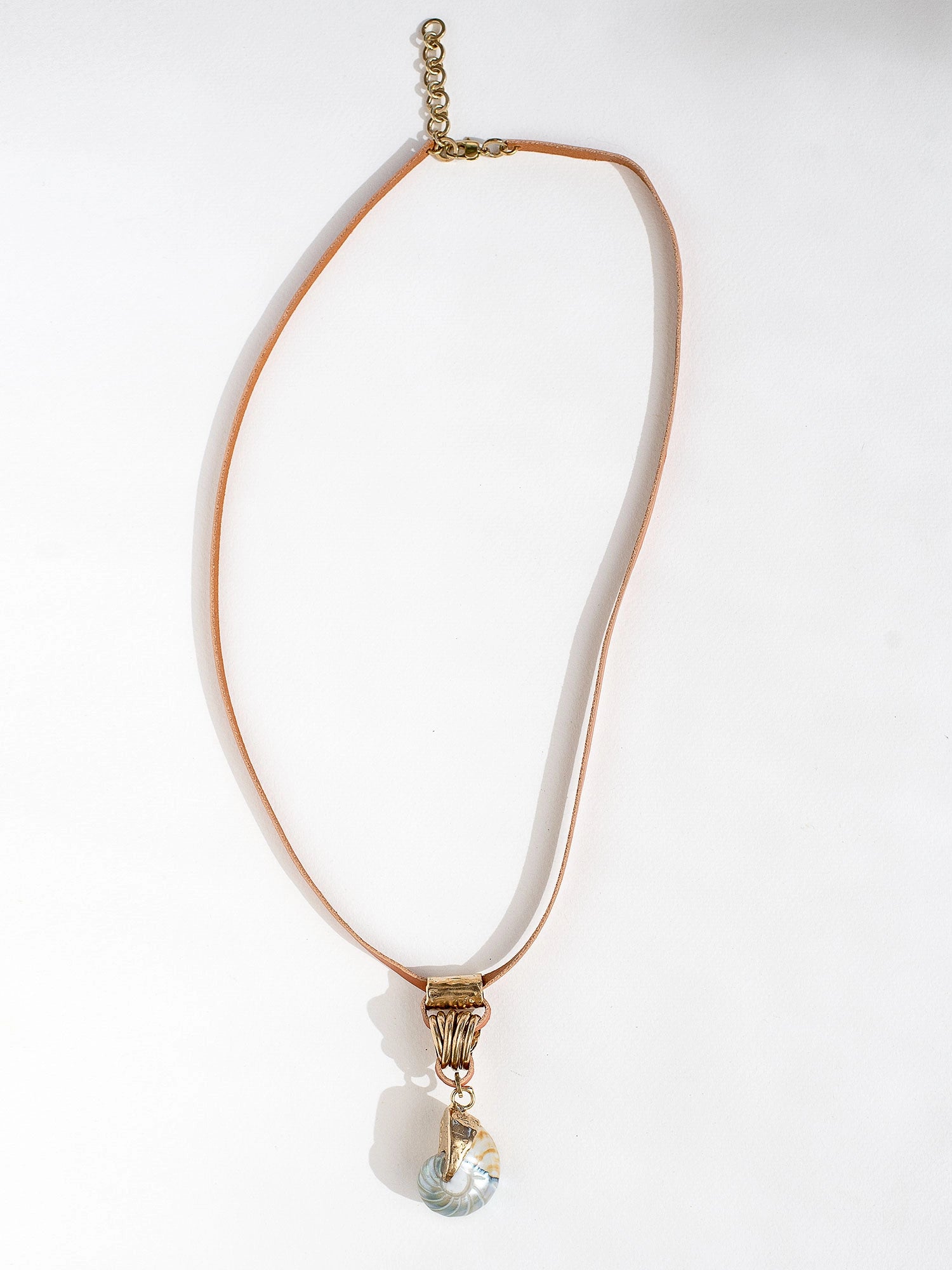 A tan leather long necklace with a brass and seashell statement pendant by Canadian jewelry designer Michelle Ross