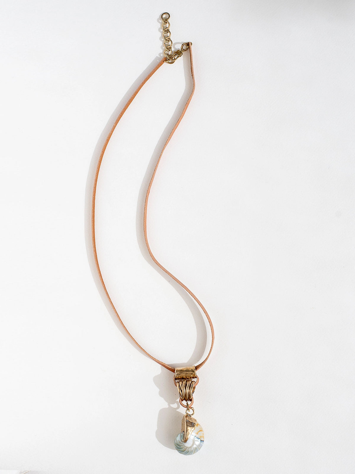A tan leather long necklace with a brass and seashell statement pendant by Canadian jewelry designer Michelle Ross