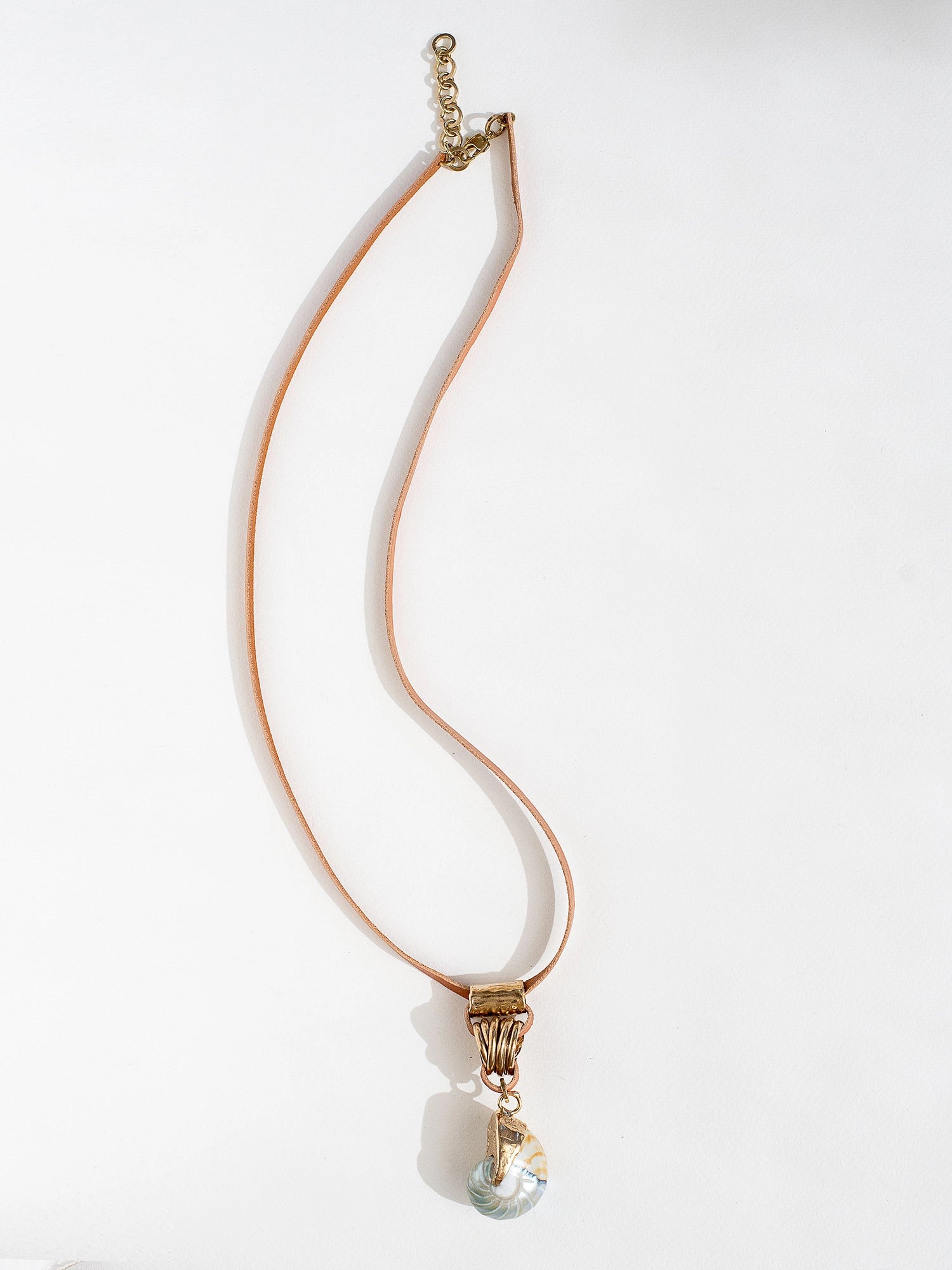 A tan leather long necklace with a brass and seashell statement pendant by Canadian jewelry designer Michelle Ross