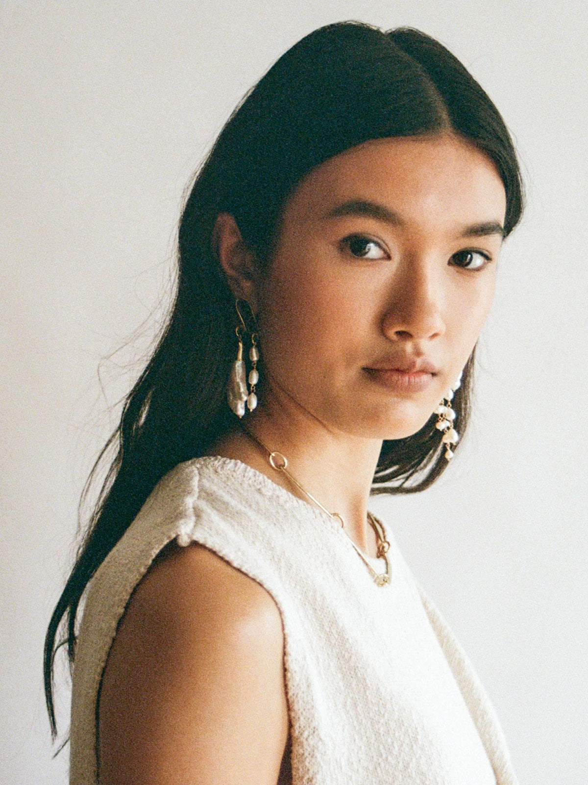 Woman wears the Caito Pearl and Brass Dangle Asymmetrical Statement Earrings by Michelle Ross