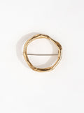A gold-colored, hand formed solid brass brooch with a circular shape and a pin