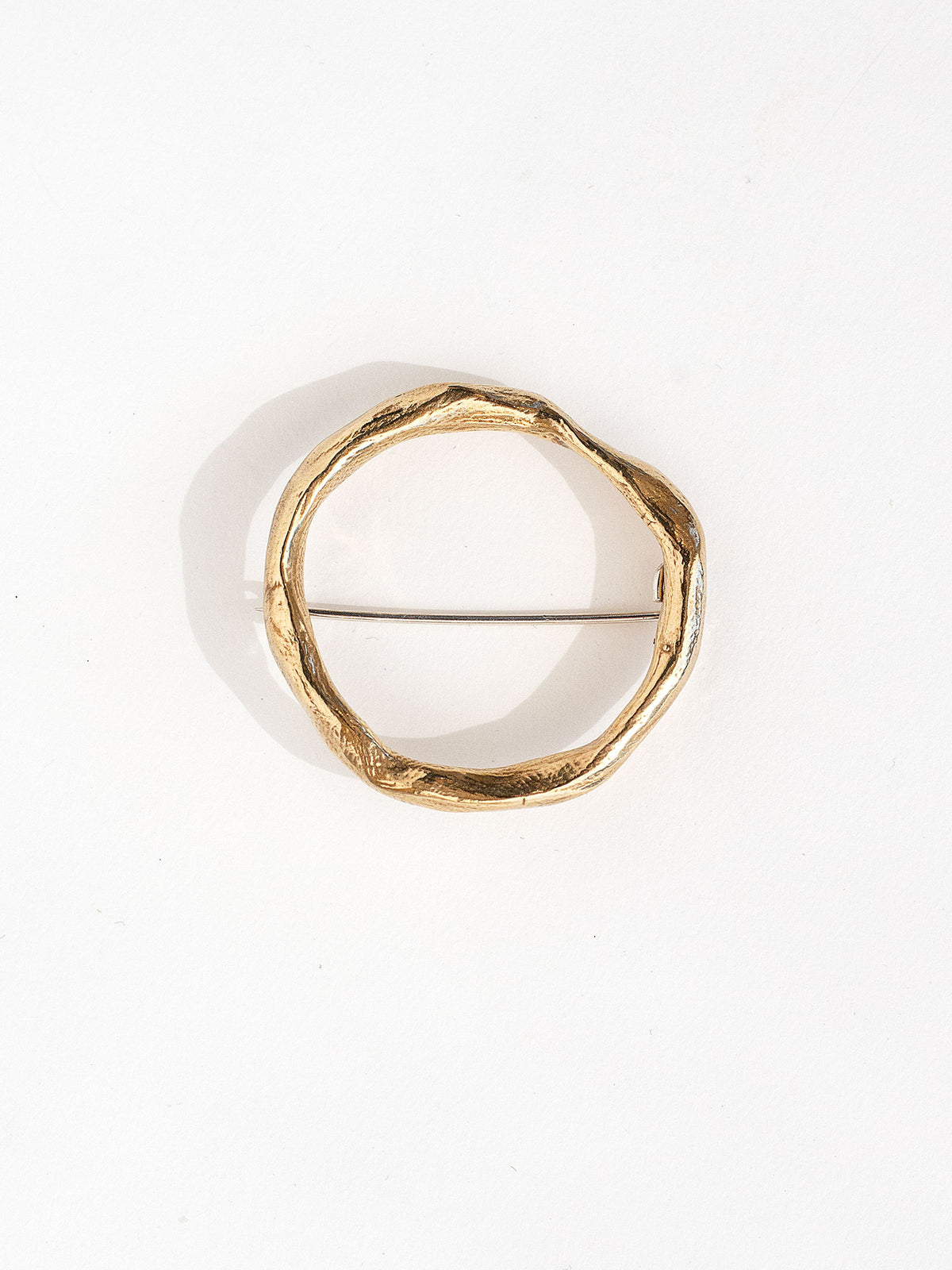 A gold-colored, hand formed solid brass brooch with a circular shape and a pin