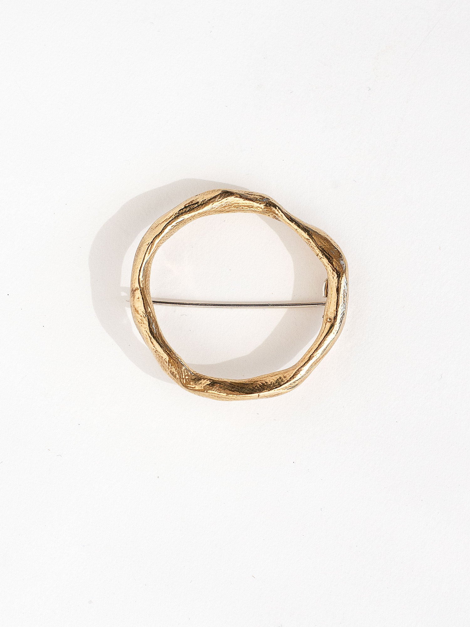 A gold-colored, hand formed solid brass brooch with a circular shape and a pin