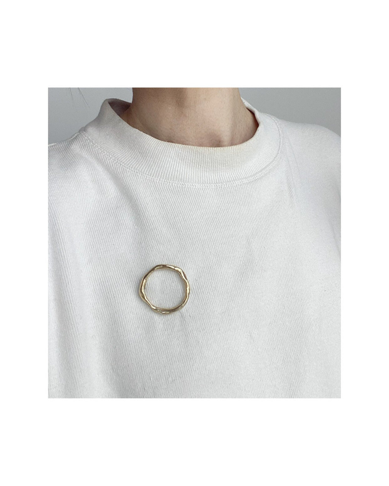 A gold-colored, hand formed solid brass brooch with a circular shape and a pin