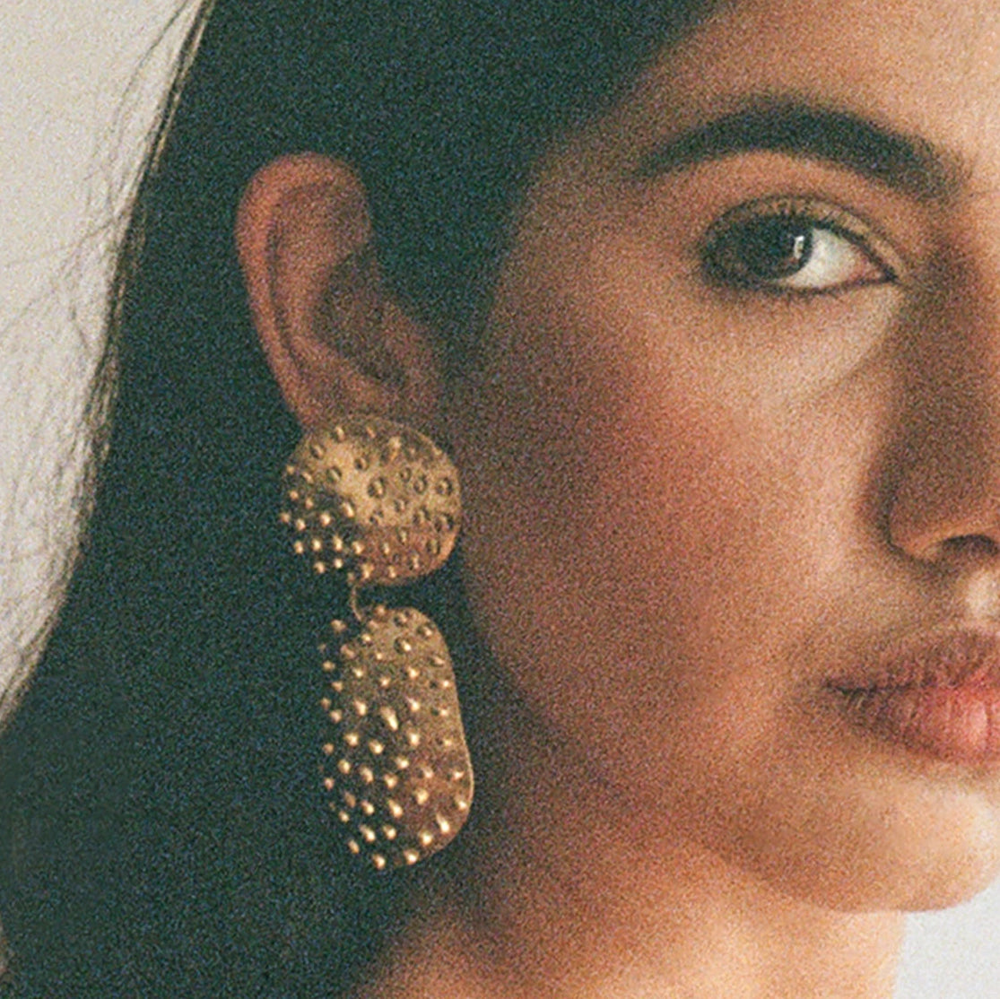 A woman wears brass statement earrings handmade by Canadian jewellery designer Michelle Ross from Toronto