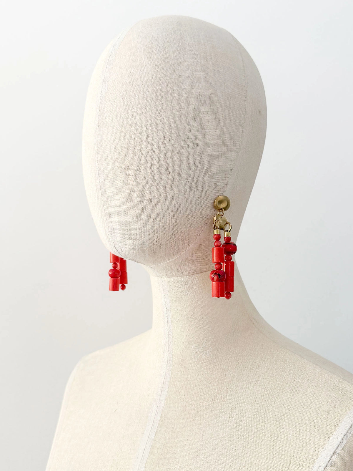 A pair of statement chandelier earrings featuring brass metal discs with vibrant red coral and resin beads by Canadian jewelry designer Michelle Ross