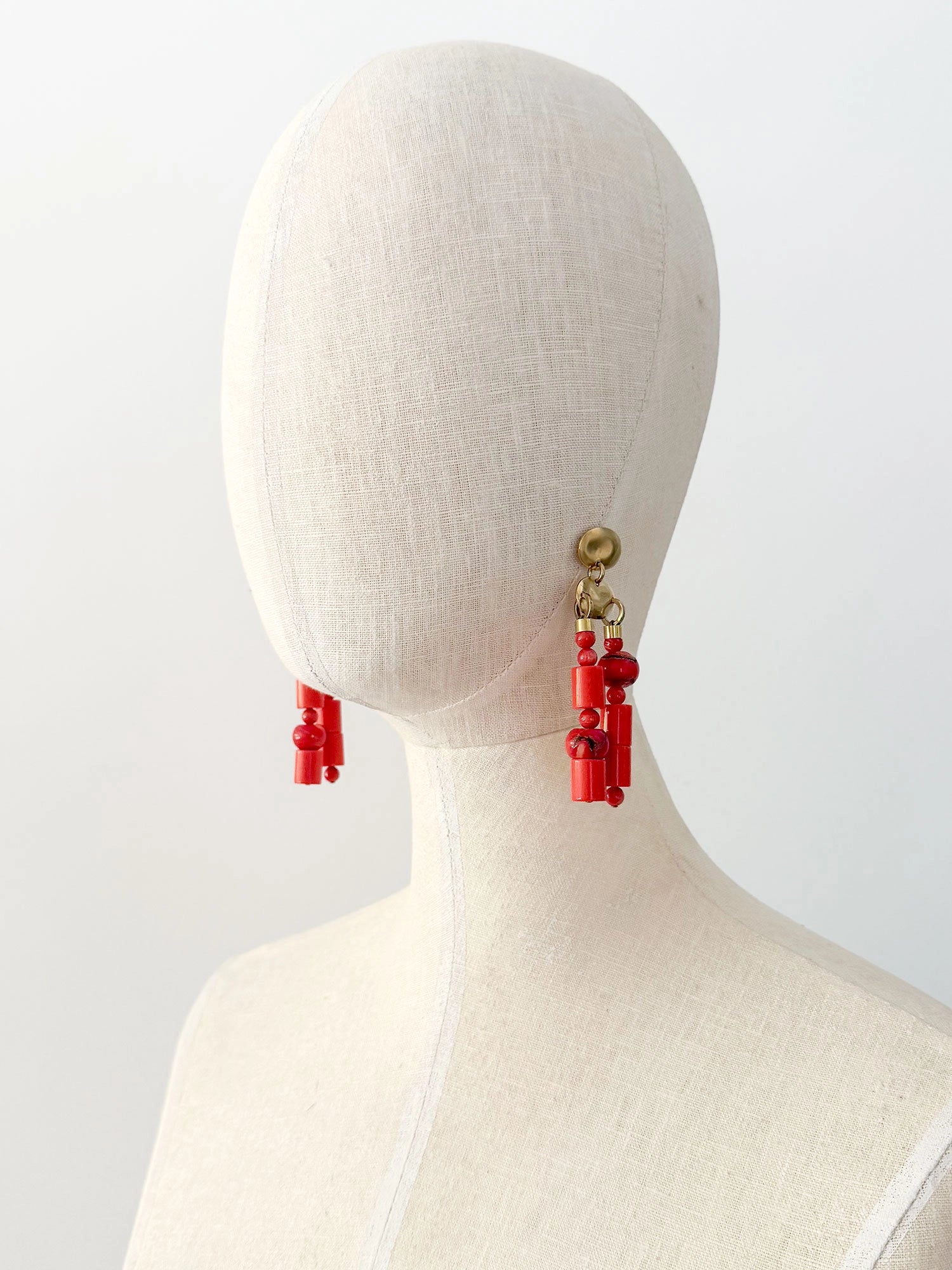 A pair of statement chandelier earrings featuring brass metal discs with vibrant red coral and resin beads by Canadian jewelry designer Michelle Ross