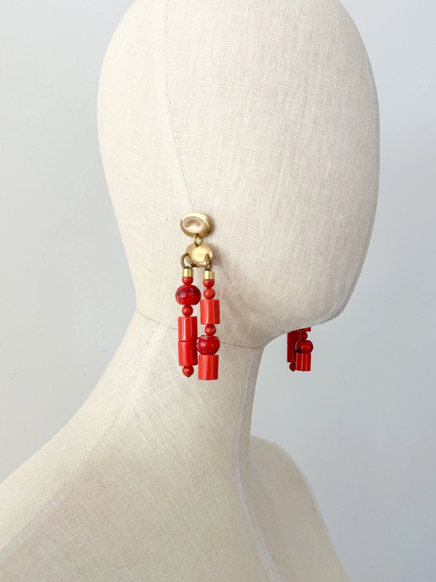 A pair of statement chandelier earrings featuring brass metal discs with vibrant red coral and resin beads by Canadian jewelry designer Michelle Ross