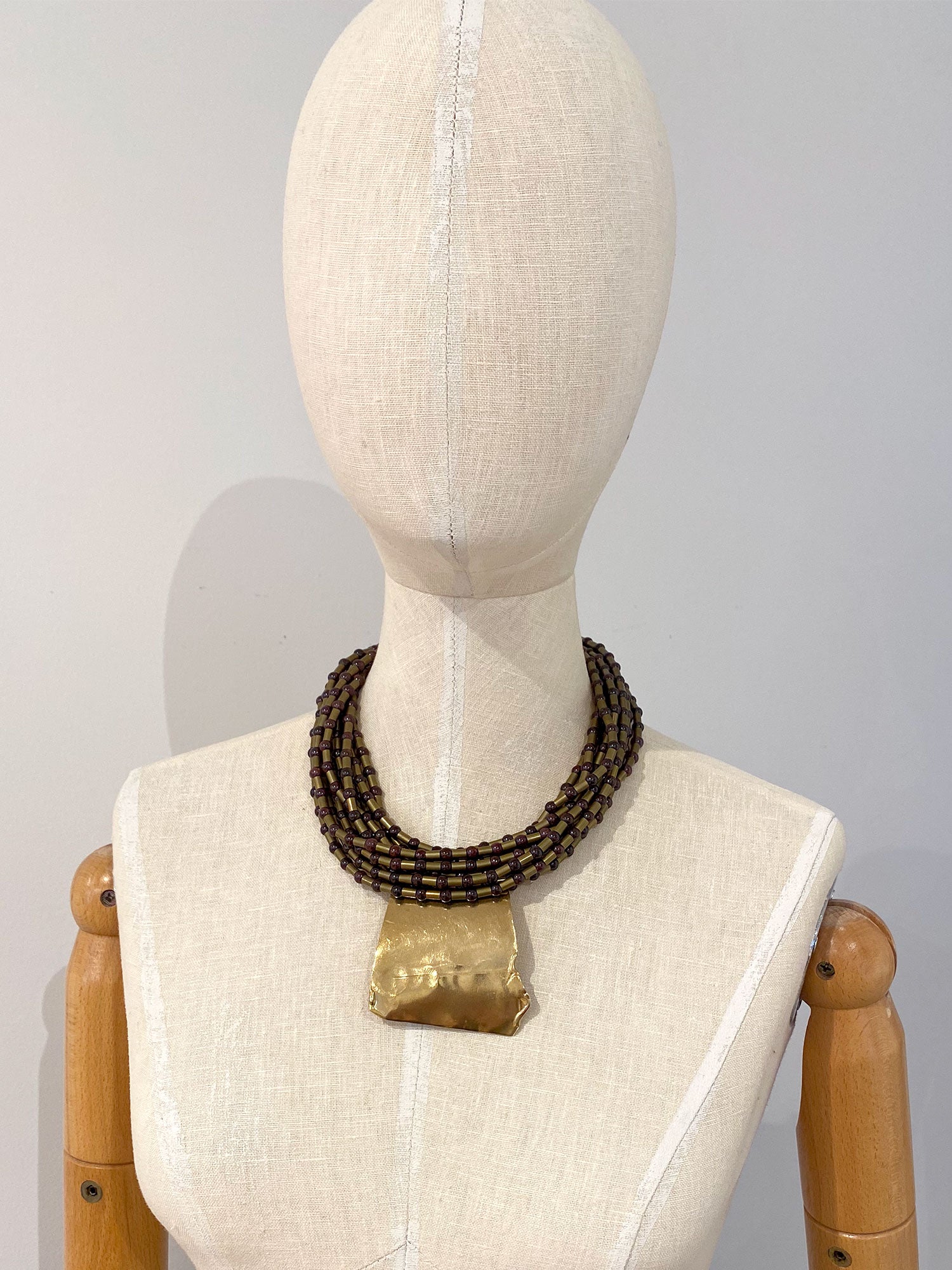 Mannequin wearing a multistrand beaded necklace with brass pendant
