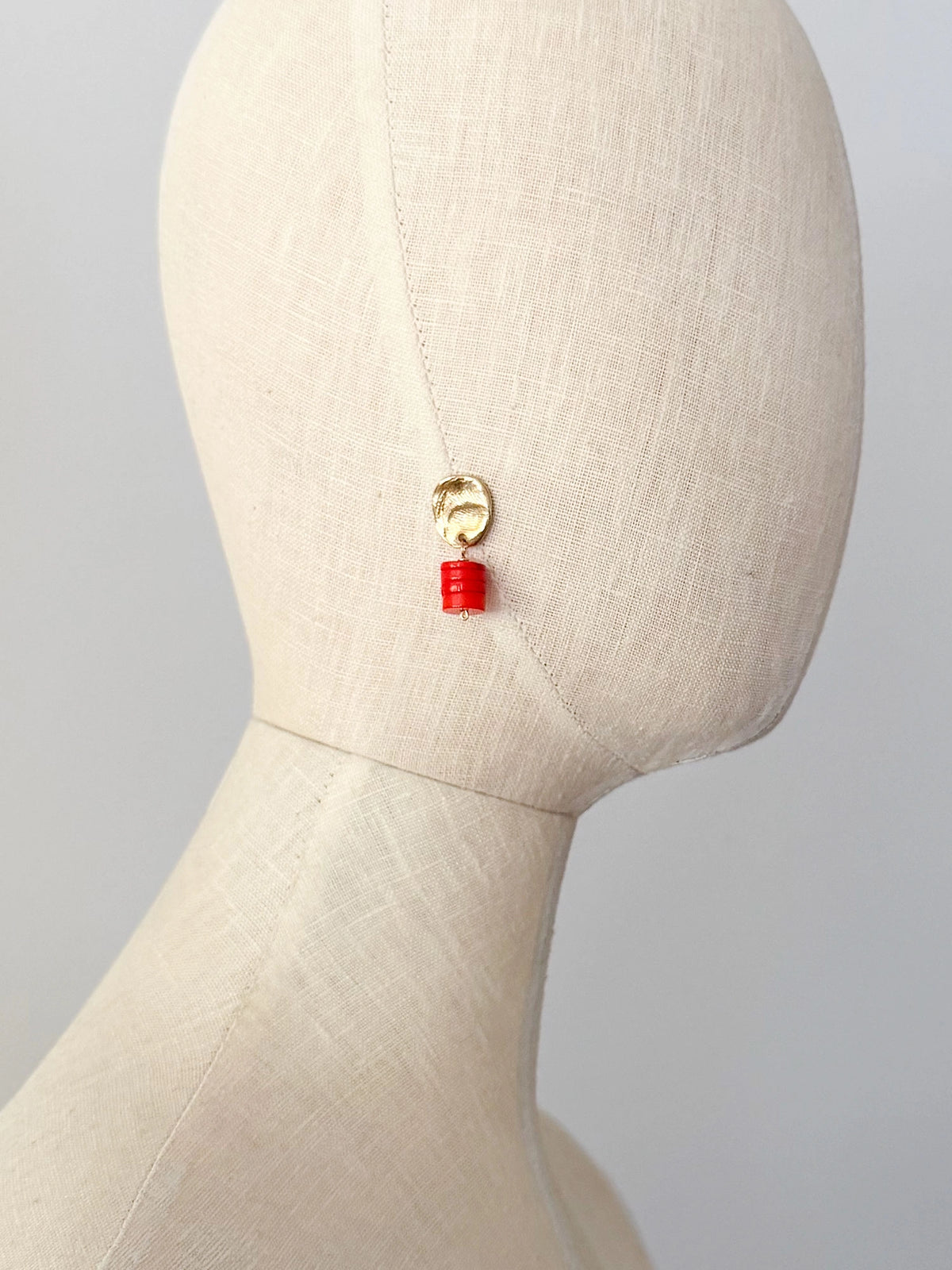 A pair of brass and orange red coral drop earrings by Canadian jewelry designer Michelle Ross. Each earring features a textured gold oval top and a stacked orange cylindrical bead drop.