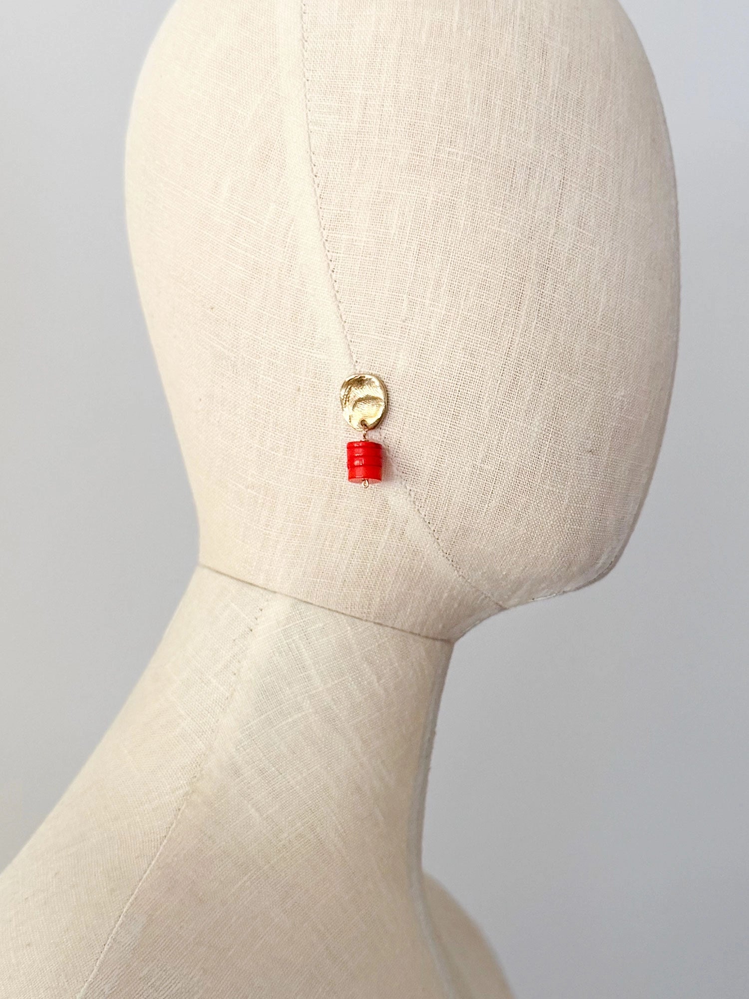 A pair of brass and orange red coral drop earrings by Canadian jewelry designer Michelle Ross. Each earring features a textured gold oval top and a stacked orange cylindrical bead drop.