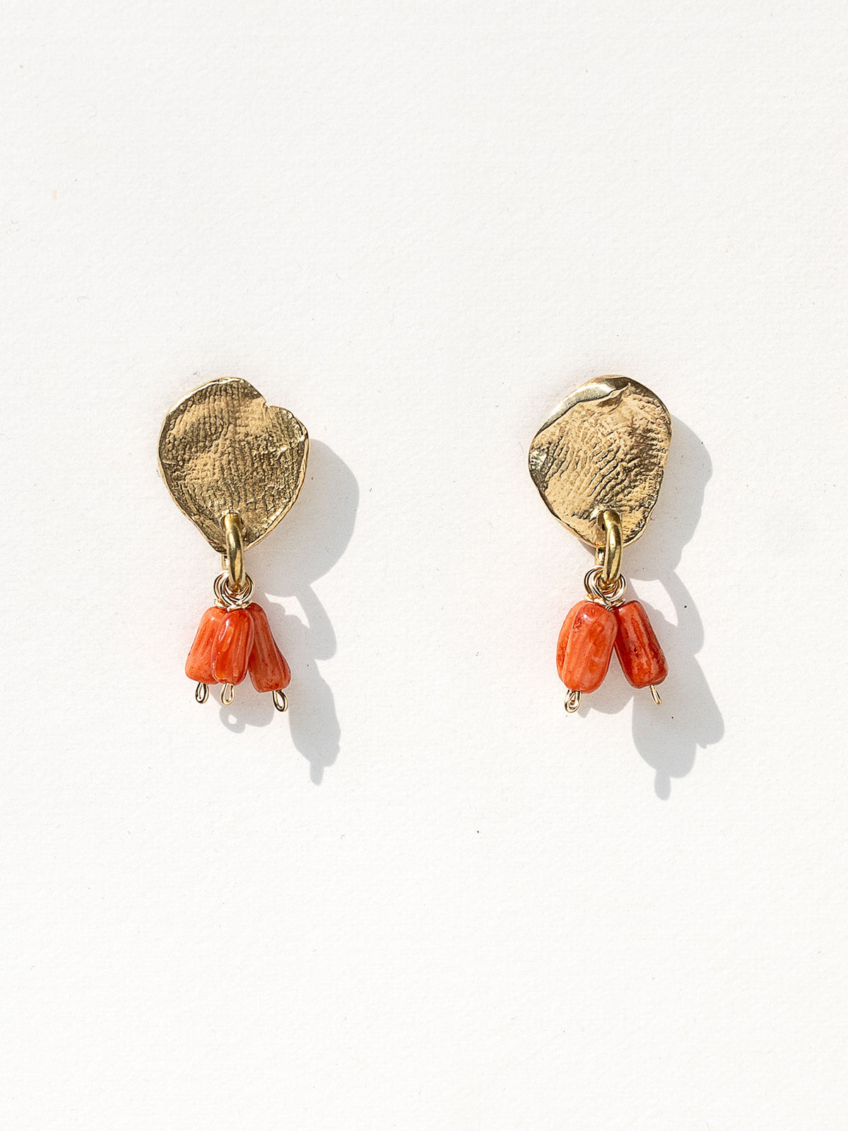 A pair of brass dangle earrings with oval coral orange bead drops by Canadian jewelry designer Michelle Ross