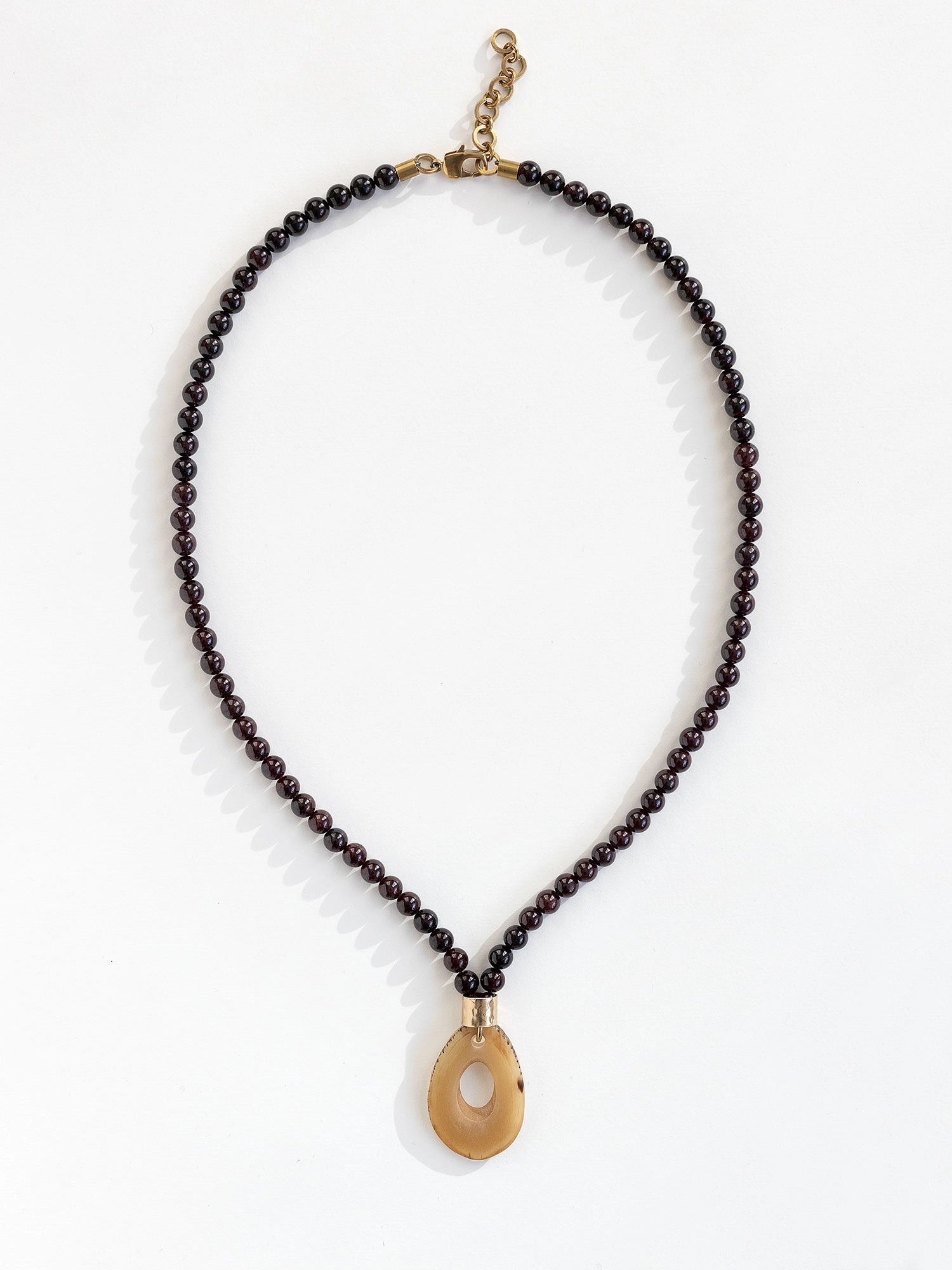 Necklace with small garnet beads and a large horn pendant with brass details by Michelle Ross