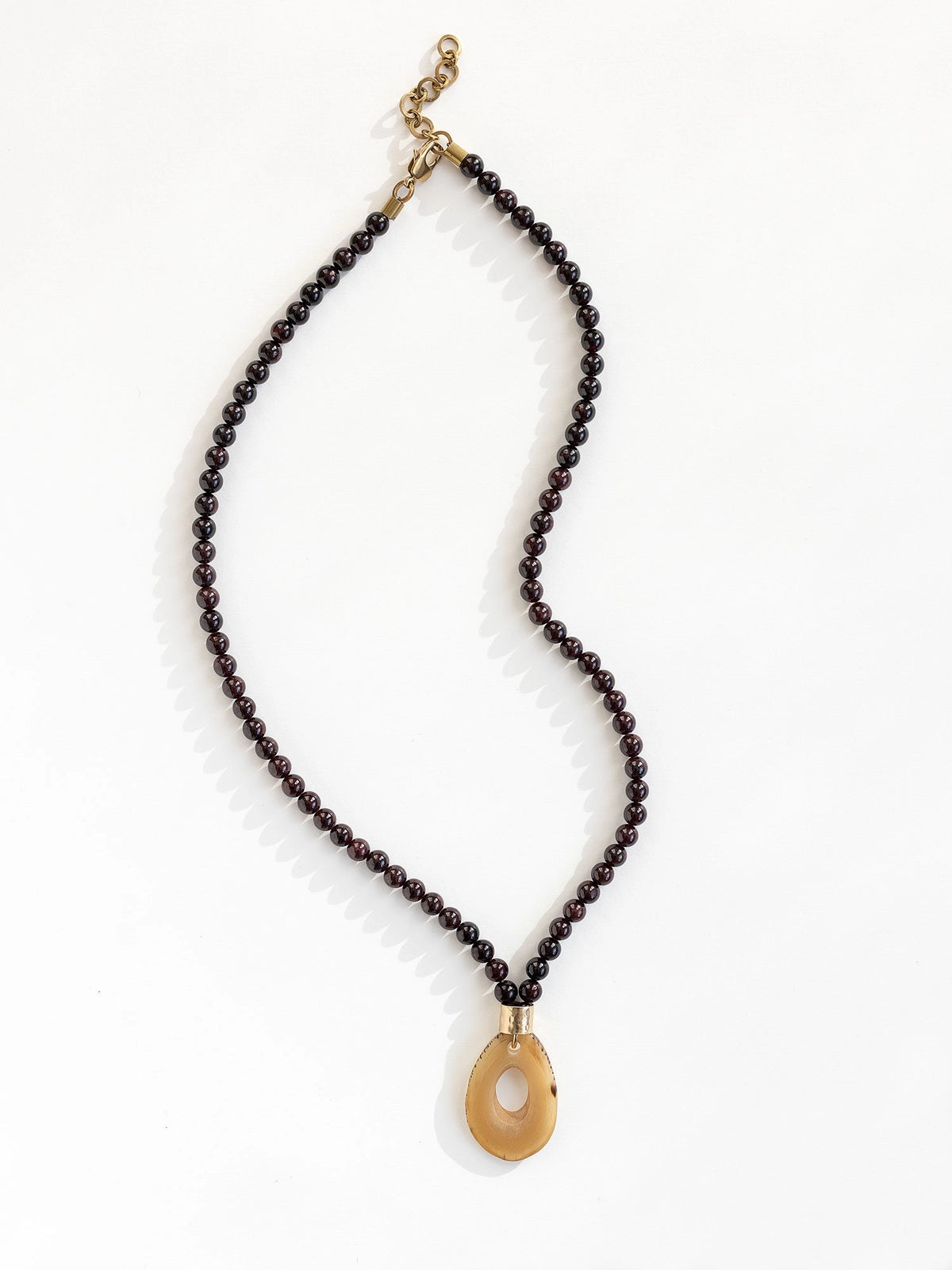 Necklace with small garnet beads and a large horn pendant with brass details by Michelle Ross