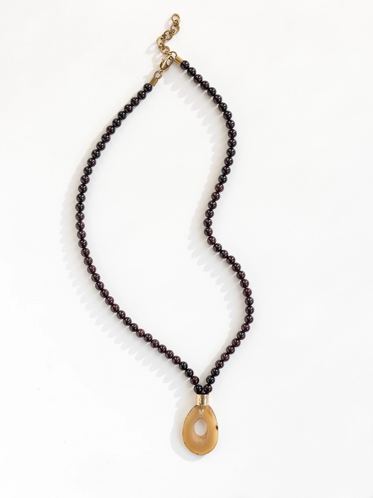 Necklace with small garnet beads and a large horn pendant with brass details by Michelle Ross