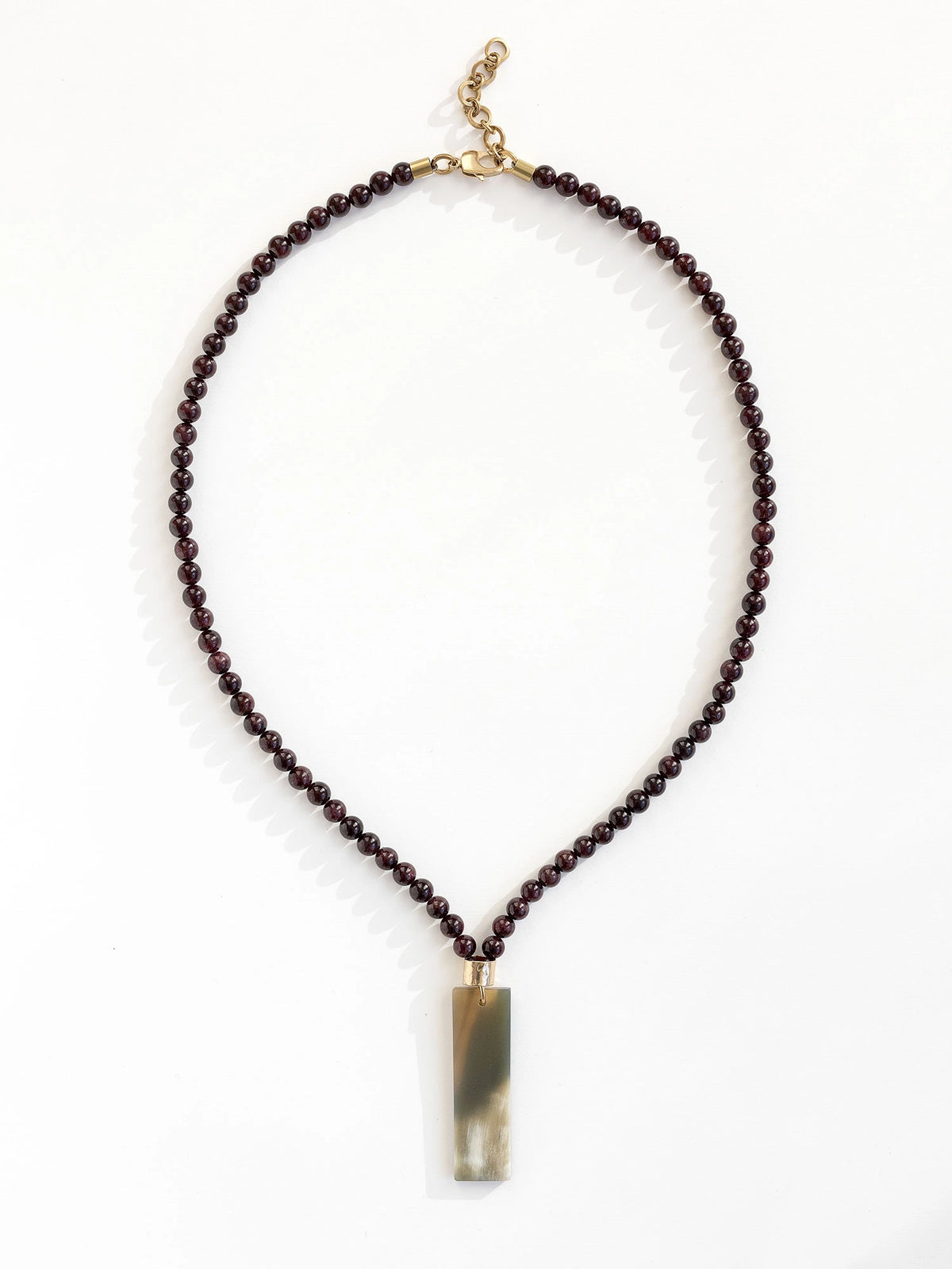 Necklace with small garnet beads and a large horn pendant with brass details by Michelle Ross