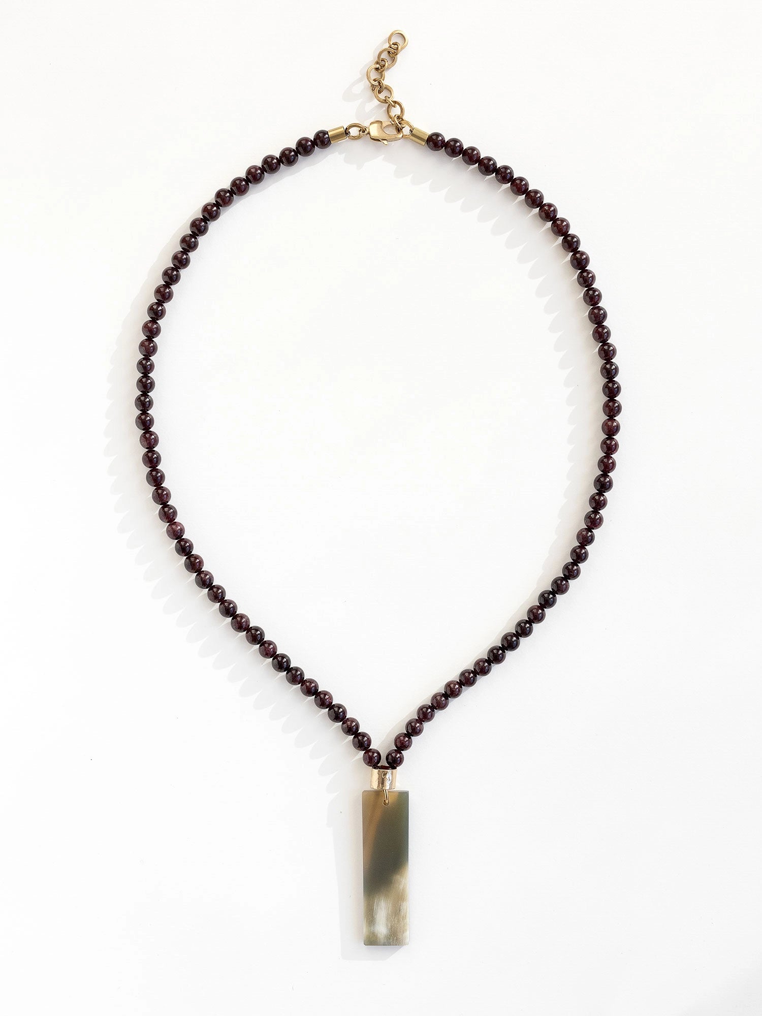 Necklace with small garnet beads and a large horn pendant with brass details by Michelle Ross