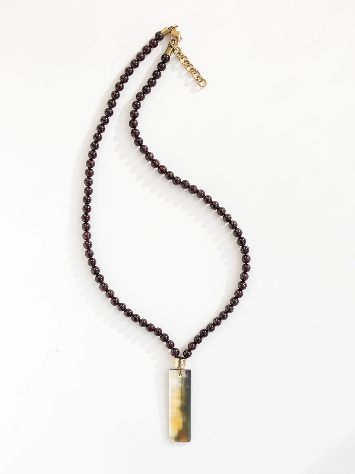 Necklace with small garnet beads and a large horn pendant with brass details by Michelle Ross