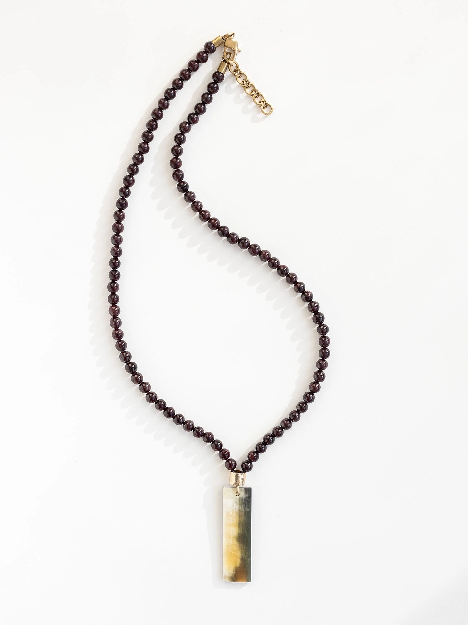 Necklace with small garnet beads and a large horn pendant with brass details by Michelle Ross