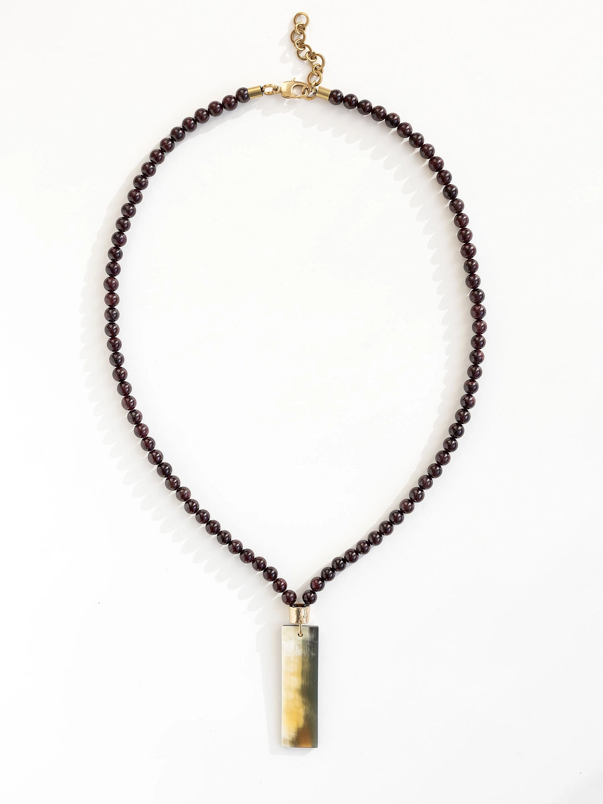 Necklace with small garnet beads and a large horn pendant with brass details by Michelle Ross