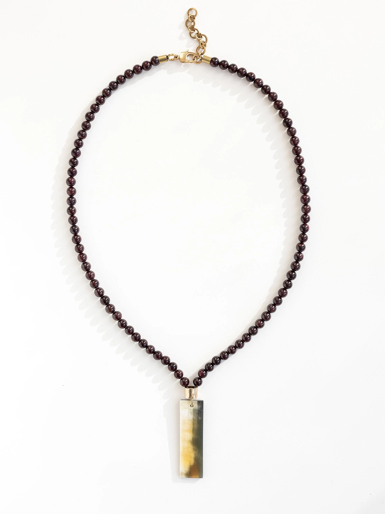 Necklace with small garnet beads and a large horn pendant with brass details by Michelle Ross