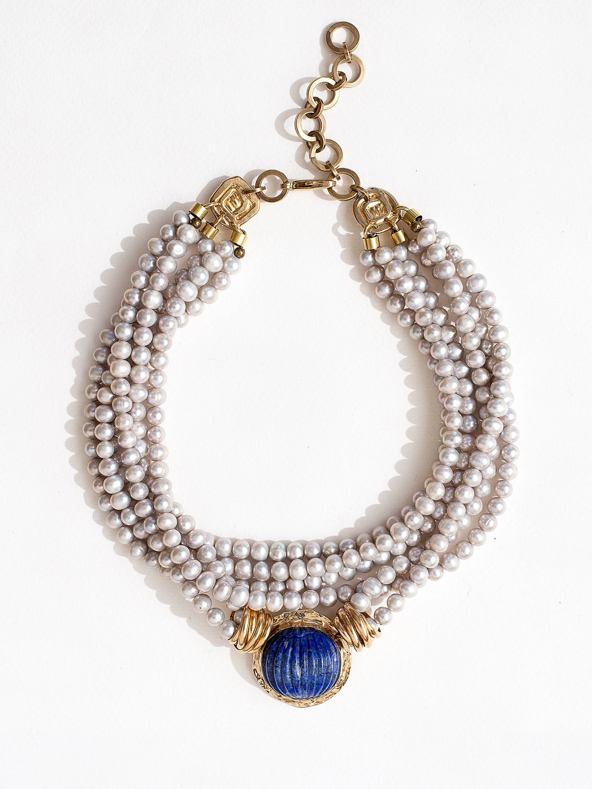 A multistrand silver pearl necklace with a large lapis lazuli and brass pendant with brass closure details by Canadian jewelry designer Michelle Ross