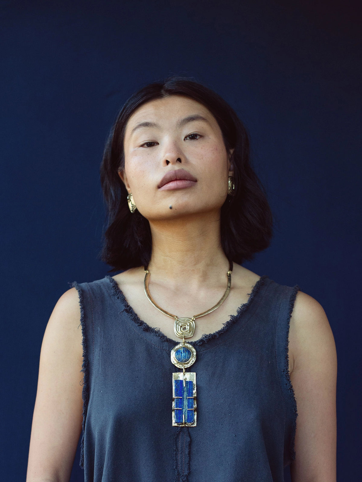 A woman wears a solid brass collar necklace with a large statement lapis lazuli pendant by Canadian jewelry designer Michelle Ross