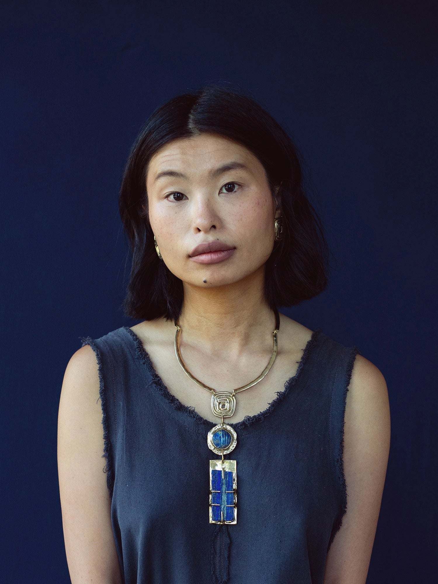 A woman wears a solid brass collar necklace with a large statement lapis lazuli pendant by Canadian jewelry designer Michelle Ross