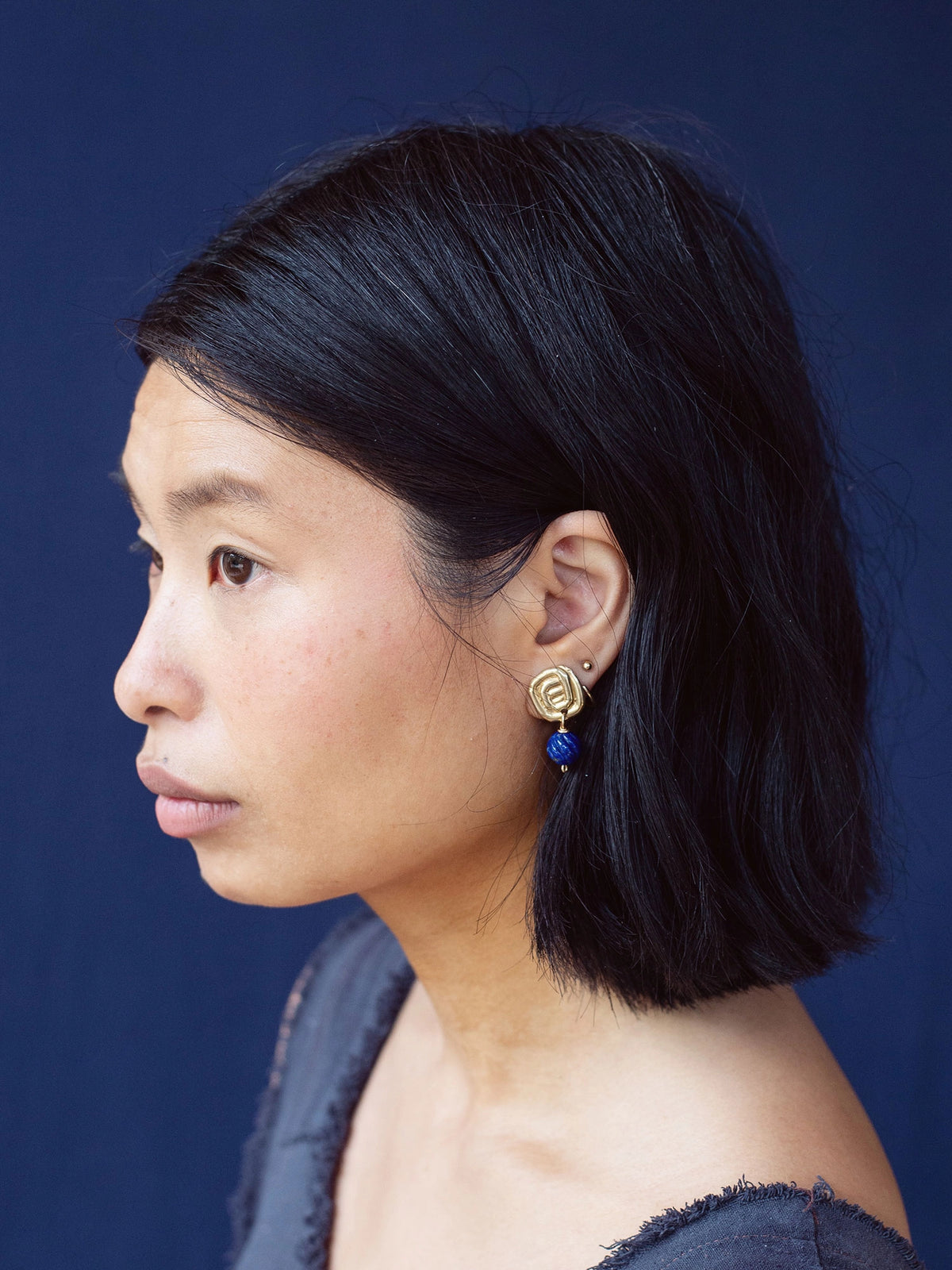 A woman wears a pair of hand-formed brass spiral drop earrings with lapis lazuli beaded stone by Canadian jewelry designer Michelle Ross